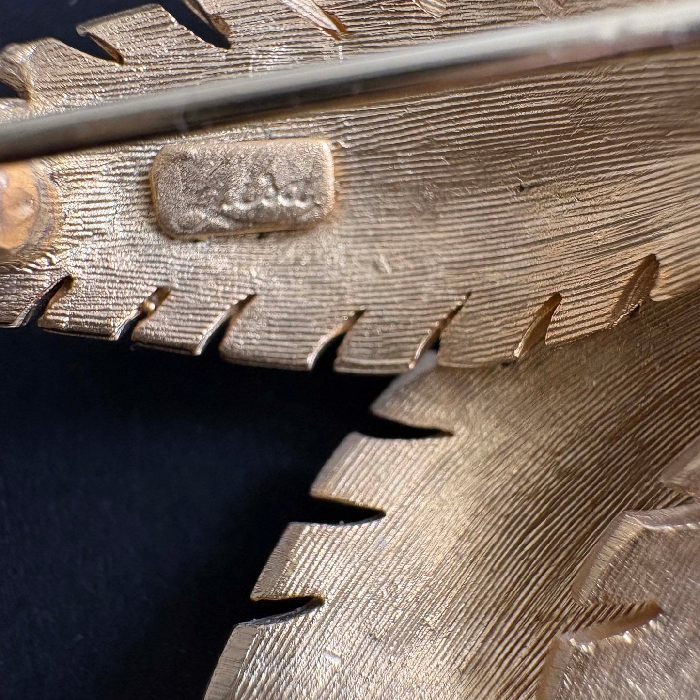 Close-up of a Lisa signature on back of brooch on a dark background