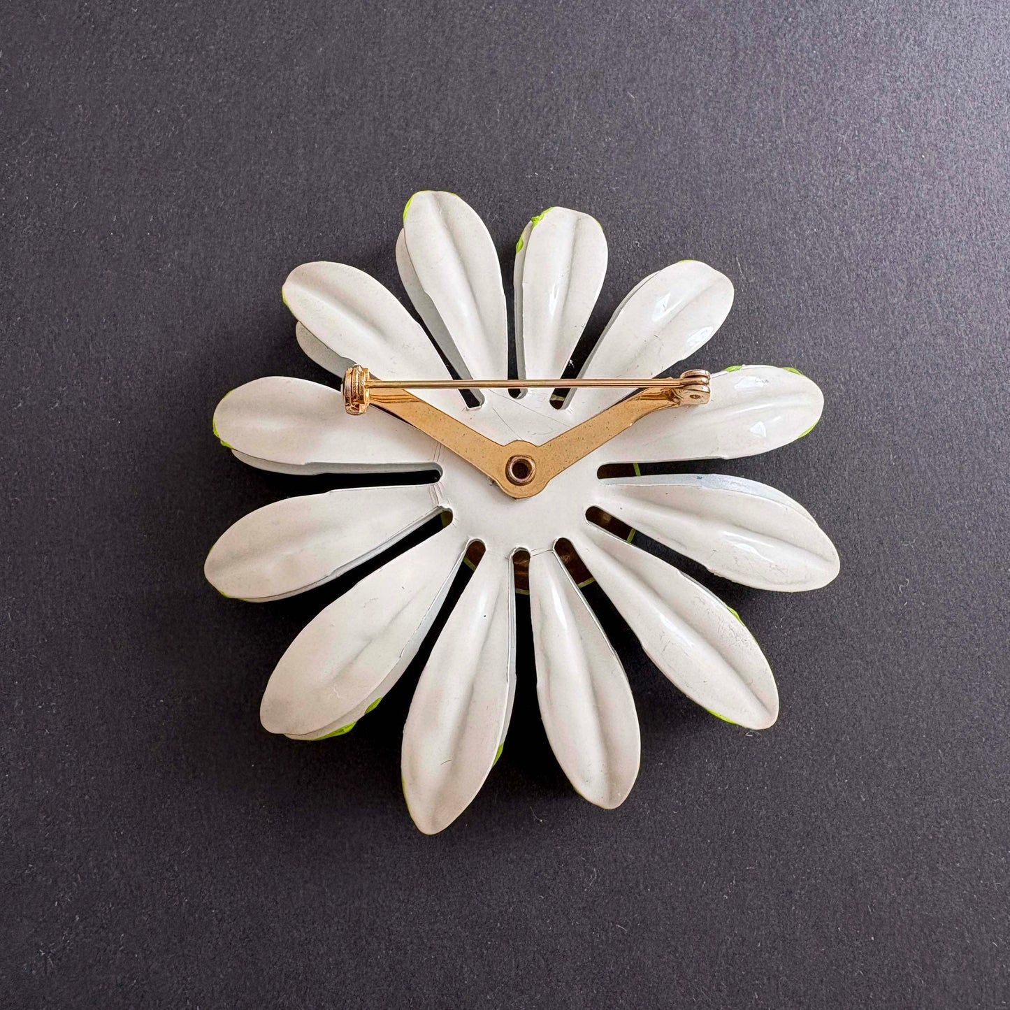 White flower-shaped brooch with gold center on a dark gray background