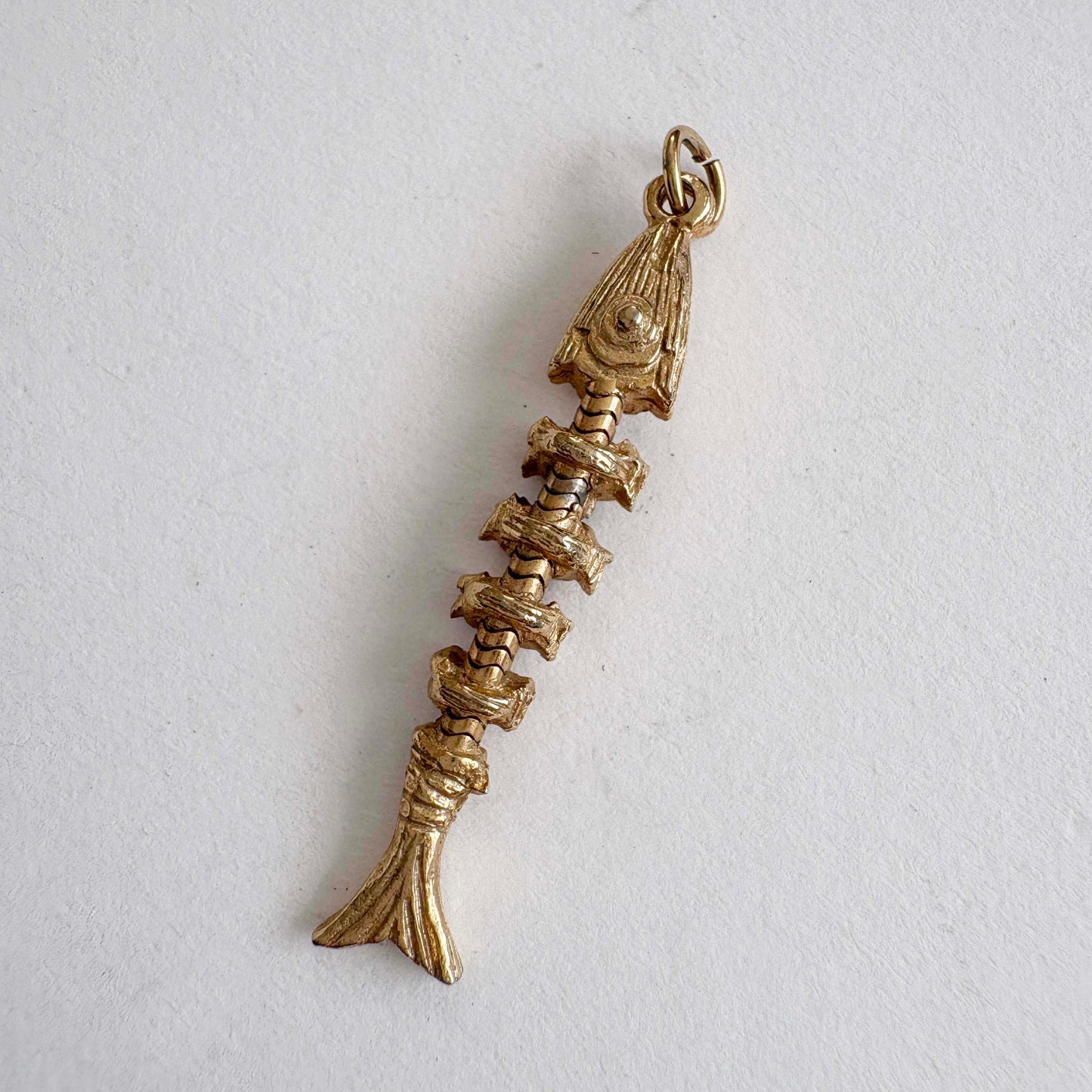 Vintage articulated gold-tone fish skeleton charm with movable segments, 1970s novelty jewelry on white background