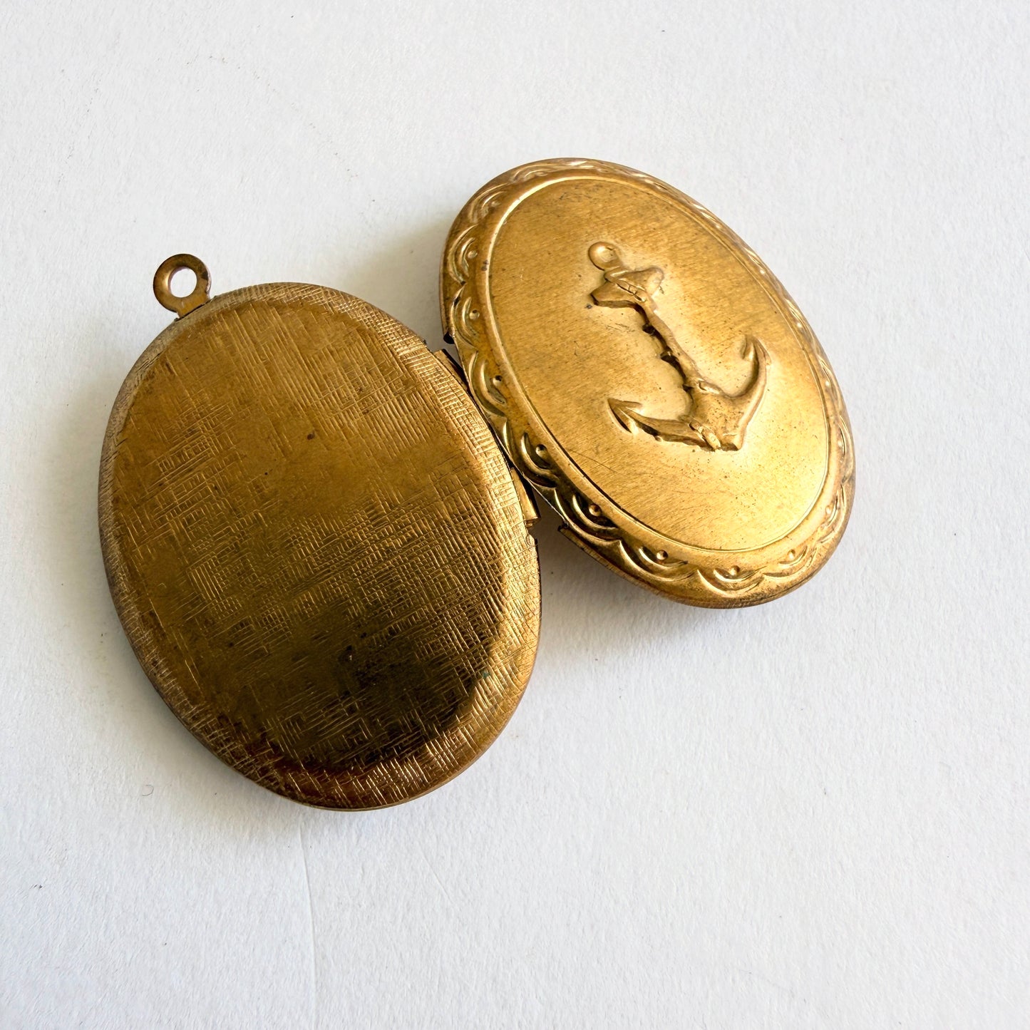 Vintage gold tone oval locket with raised anchor motif and hinged opening showing dual photo compartments, circa 1960s