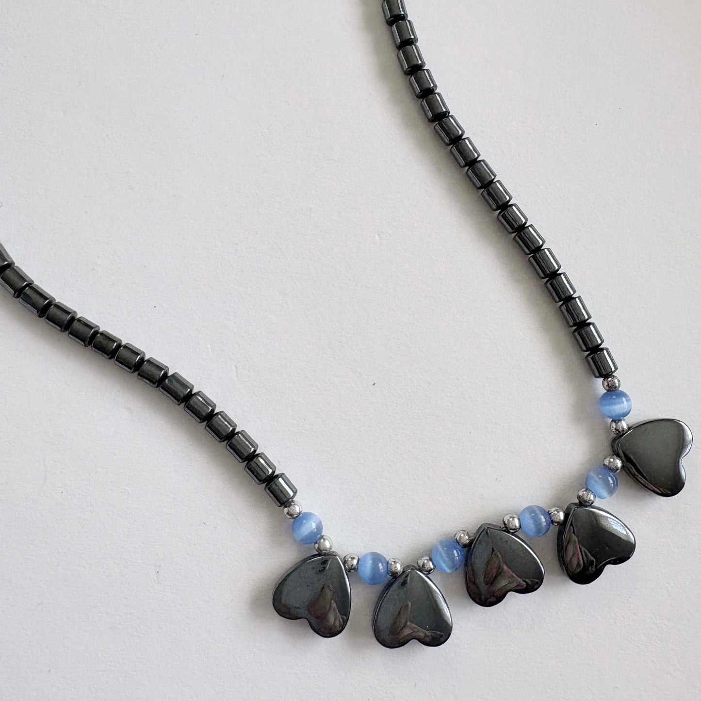 Necklace with black heart-shaped beads and blue beads on a light gray background