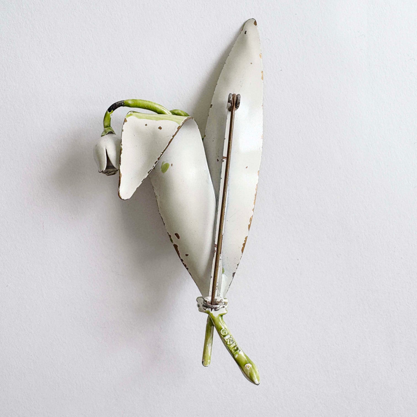 Floral brooch with white petals and green stem on a light gray background