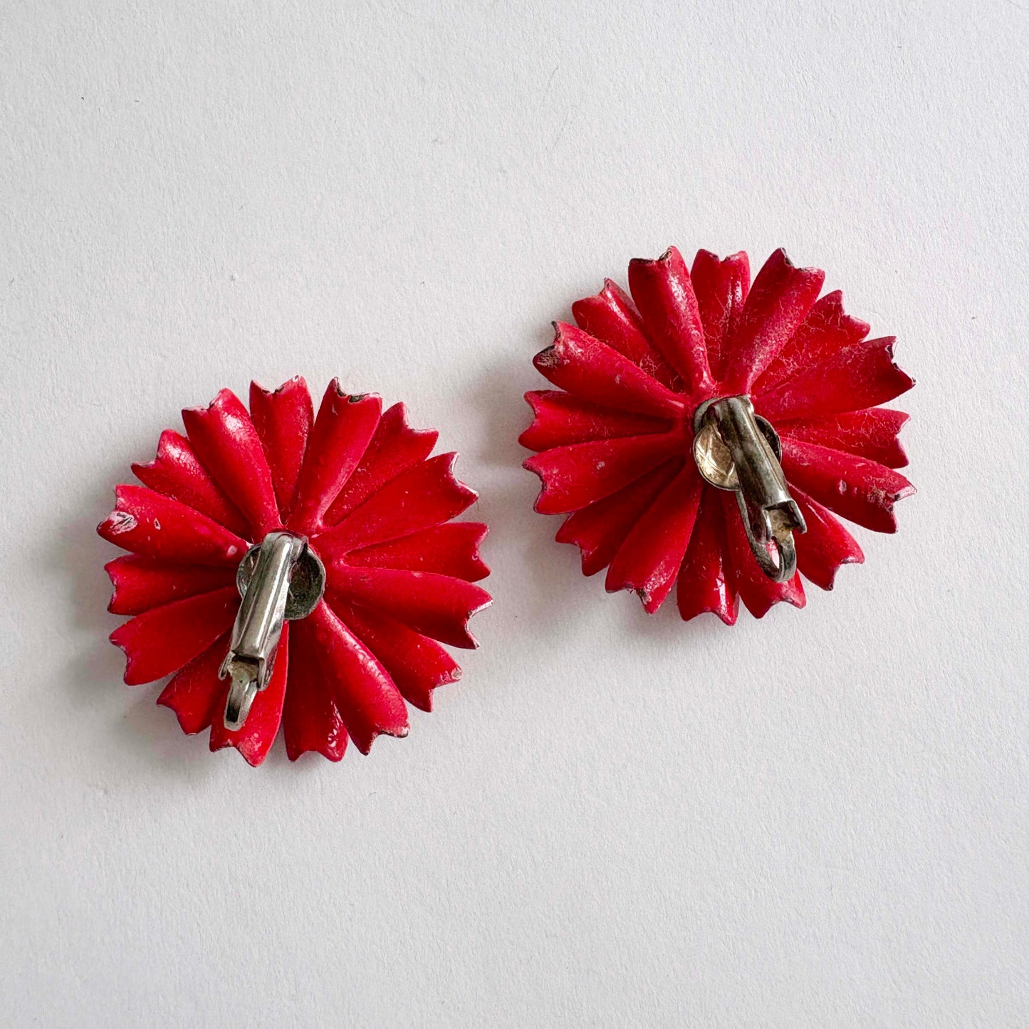 Pair of red flower-shaped clip-on earrings on a light gray background