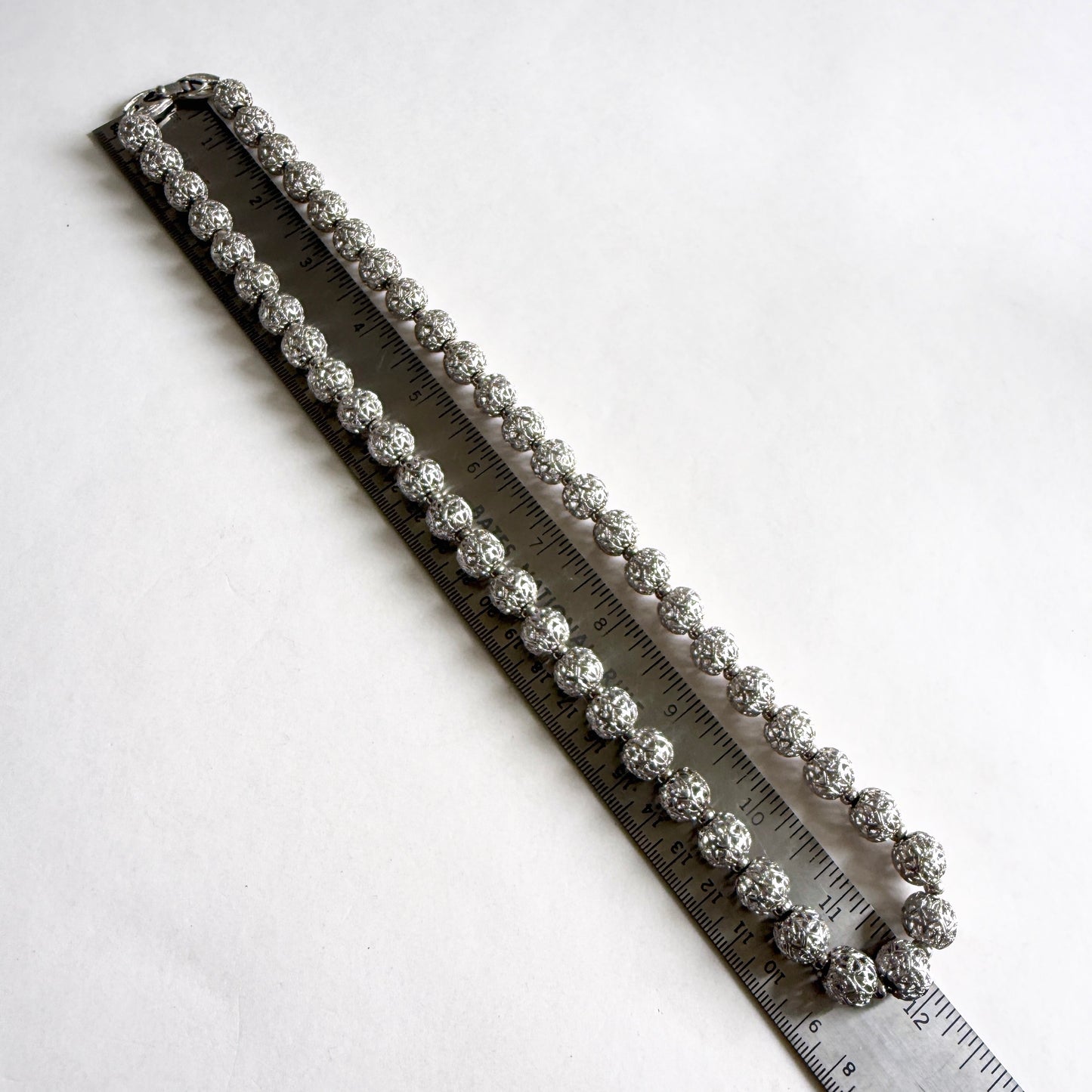 Silver bracelet on a ruler for size measurement against a white background