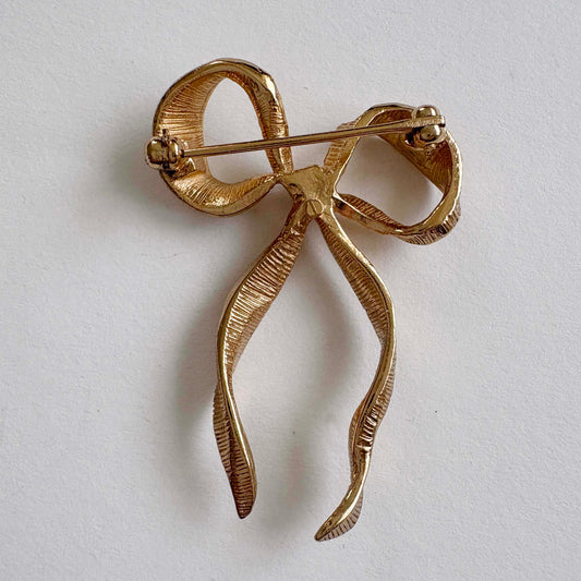 the back of a gold bow-shaped brooch on a light gray background