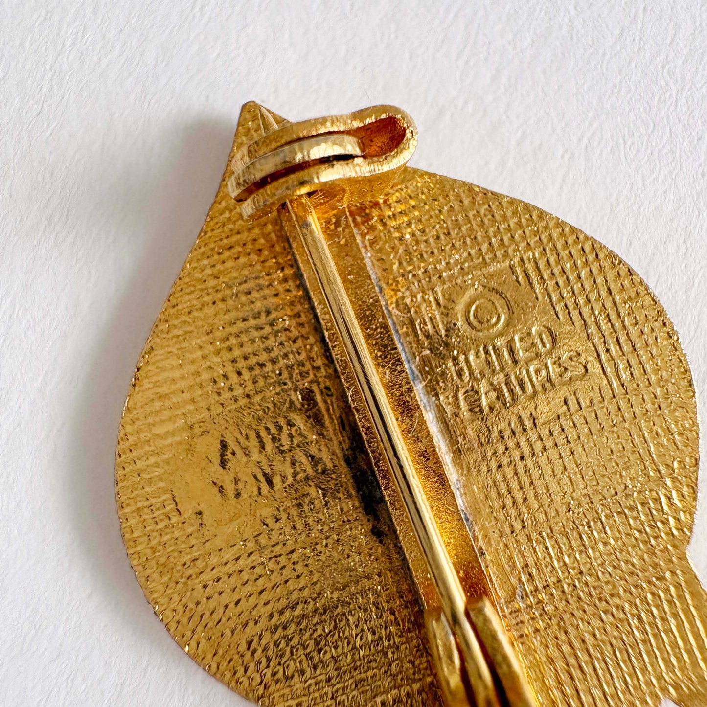 Gold pendant back with 'United Features' and AVIVA on a white background