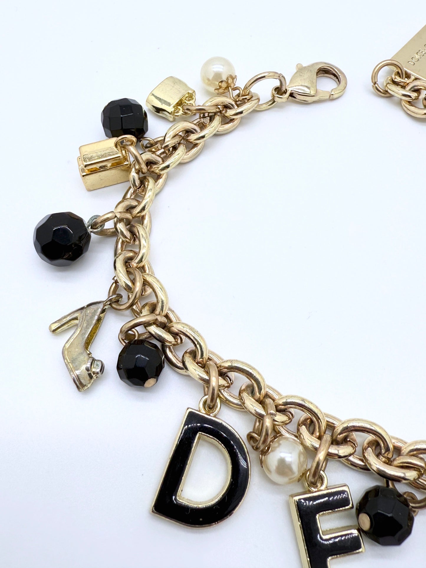 Gold charm bracelet with various charms including letters on a white background