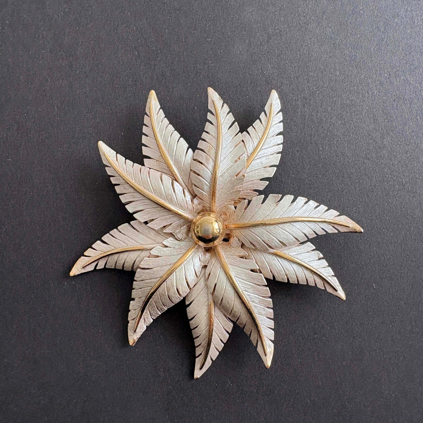 Vintage Lisa Jewels floral leaf brooch in silver and gold tones with layered metal leaves on dark background