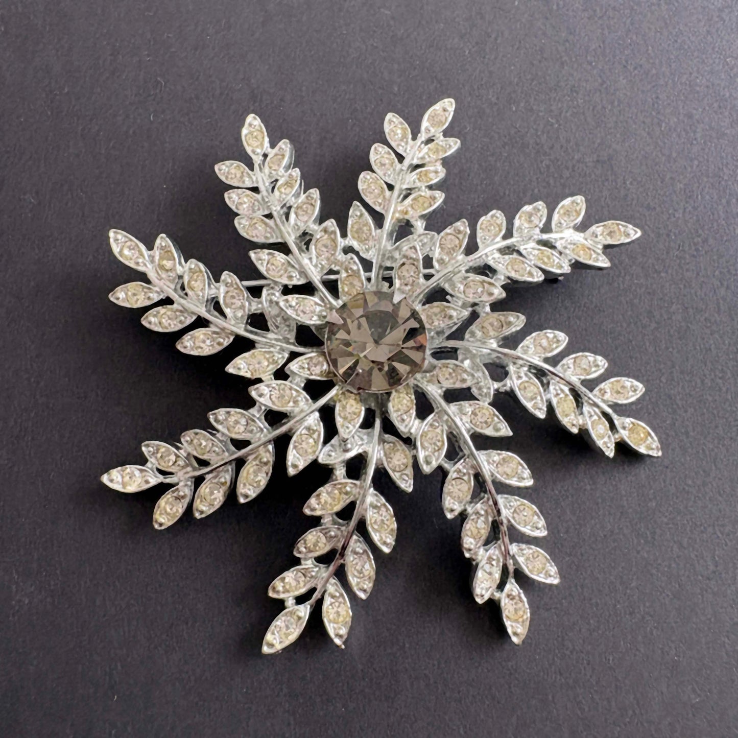 Silver snowflake-shaped brooch with gemstones on a dark background