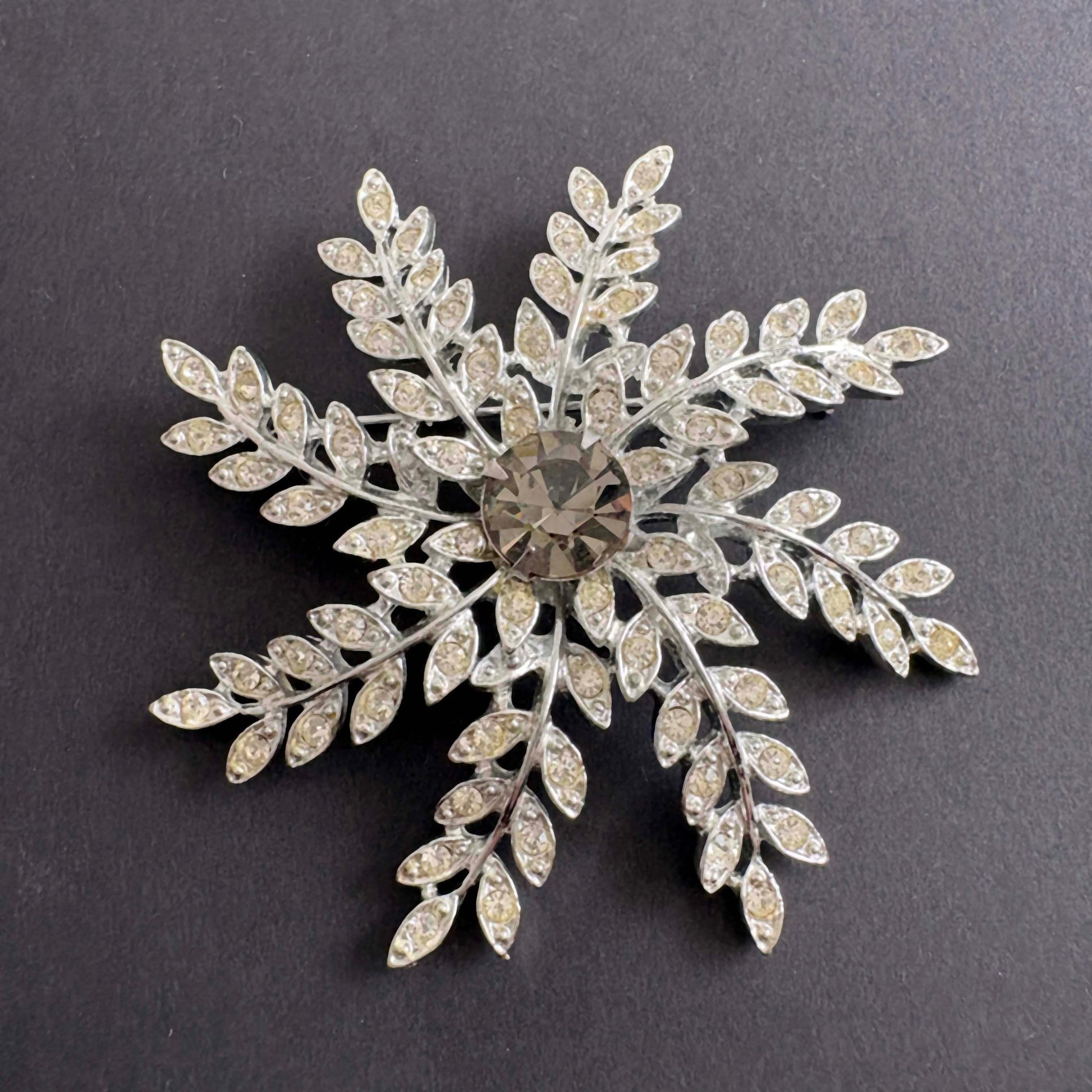 Silver snowflake-shaped brooch with gemstones on a dark background