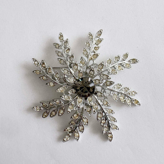 Vintage Sarah Coventry silver tone rhinestone snowflake brooch with central faceted stone on gray background