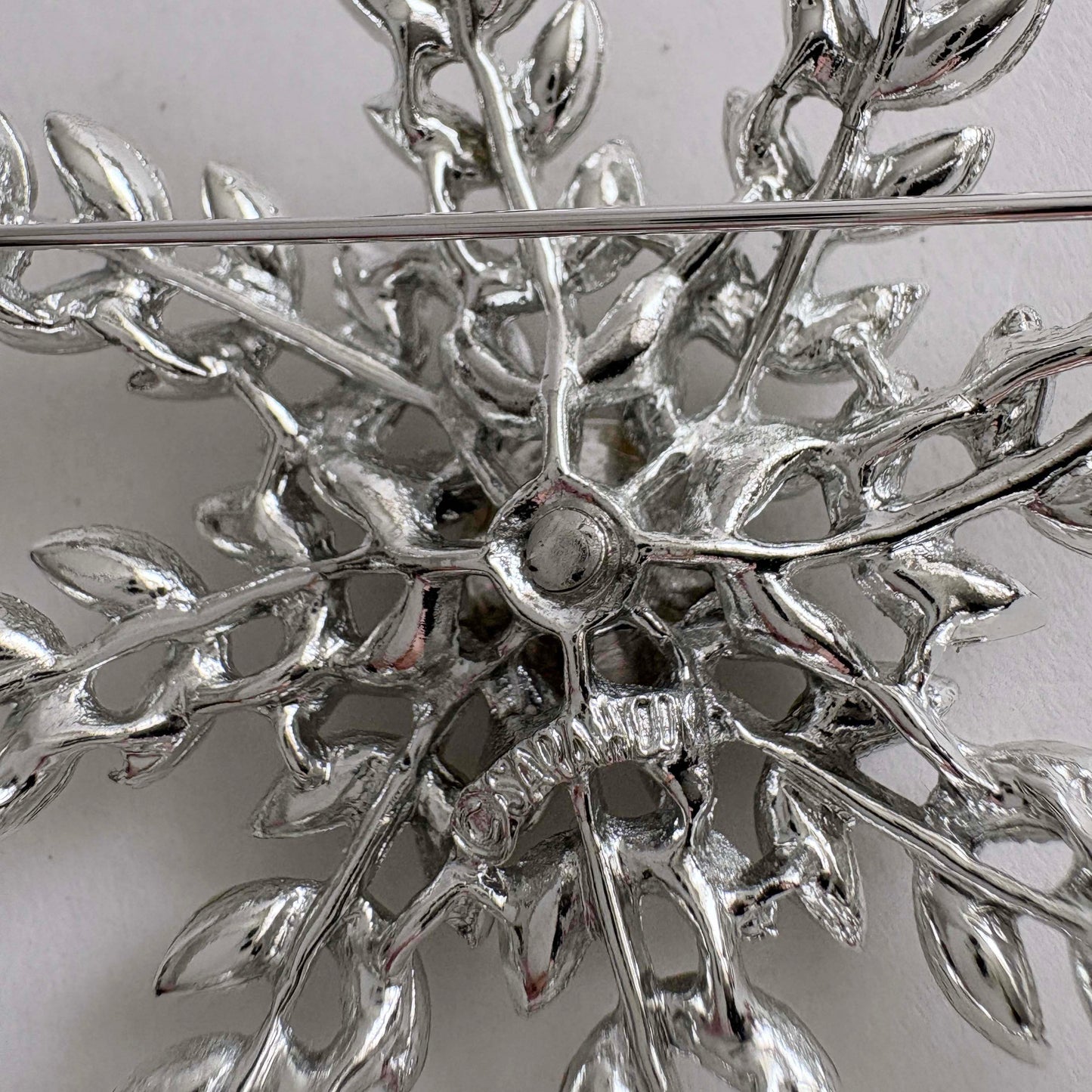 Close-up of a silver brooch with intricate leaf design and signature on a white background