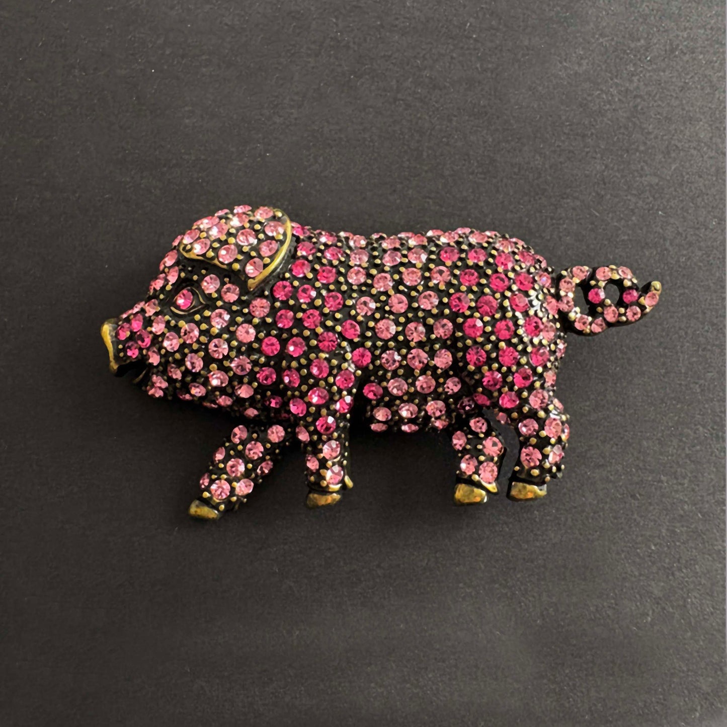 Pig-shaped jewelry with pink gemstones on a dark background