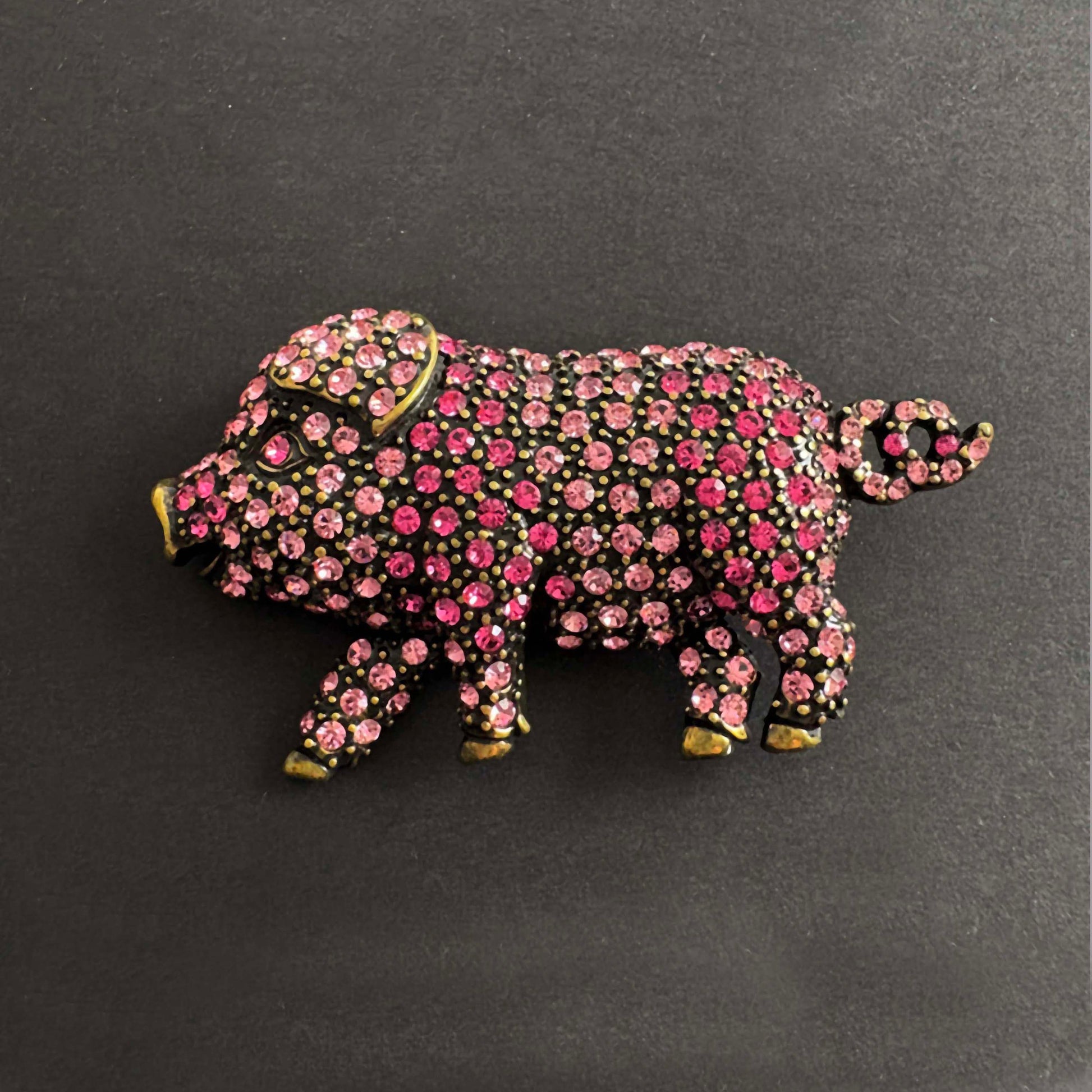 Pig-shaped jewelry with pink gemstones on a dark background