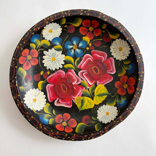 Vintage hand-painted Mexican wooden batea tray with colorful floral folk art on a black background, round decorative bowl
