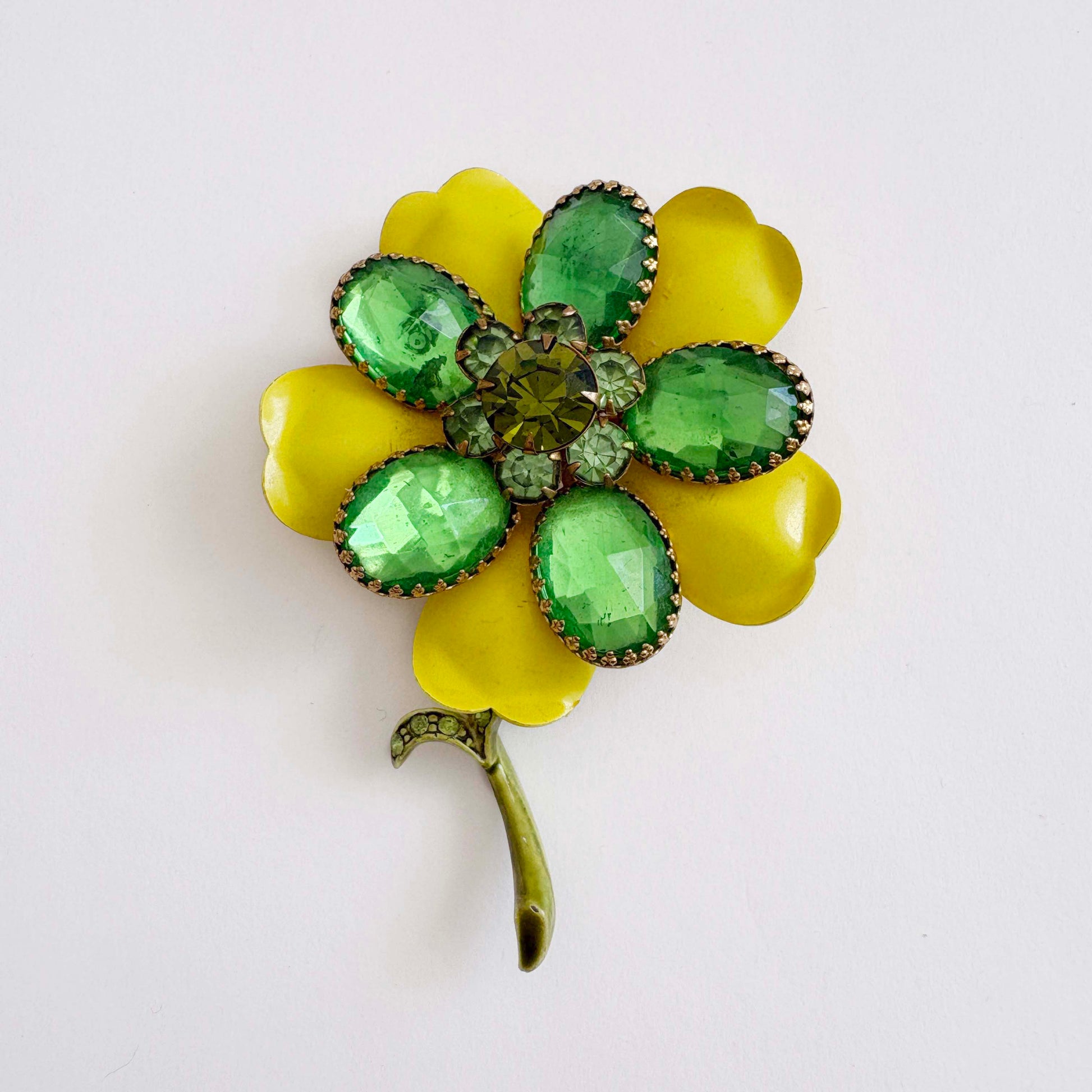 Floral brooch with green gemstones and yellow petals on a white background