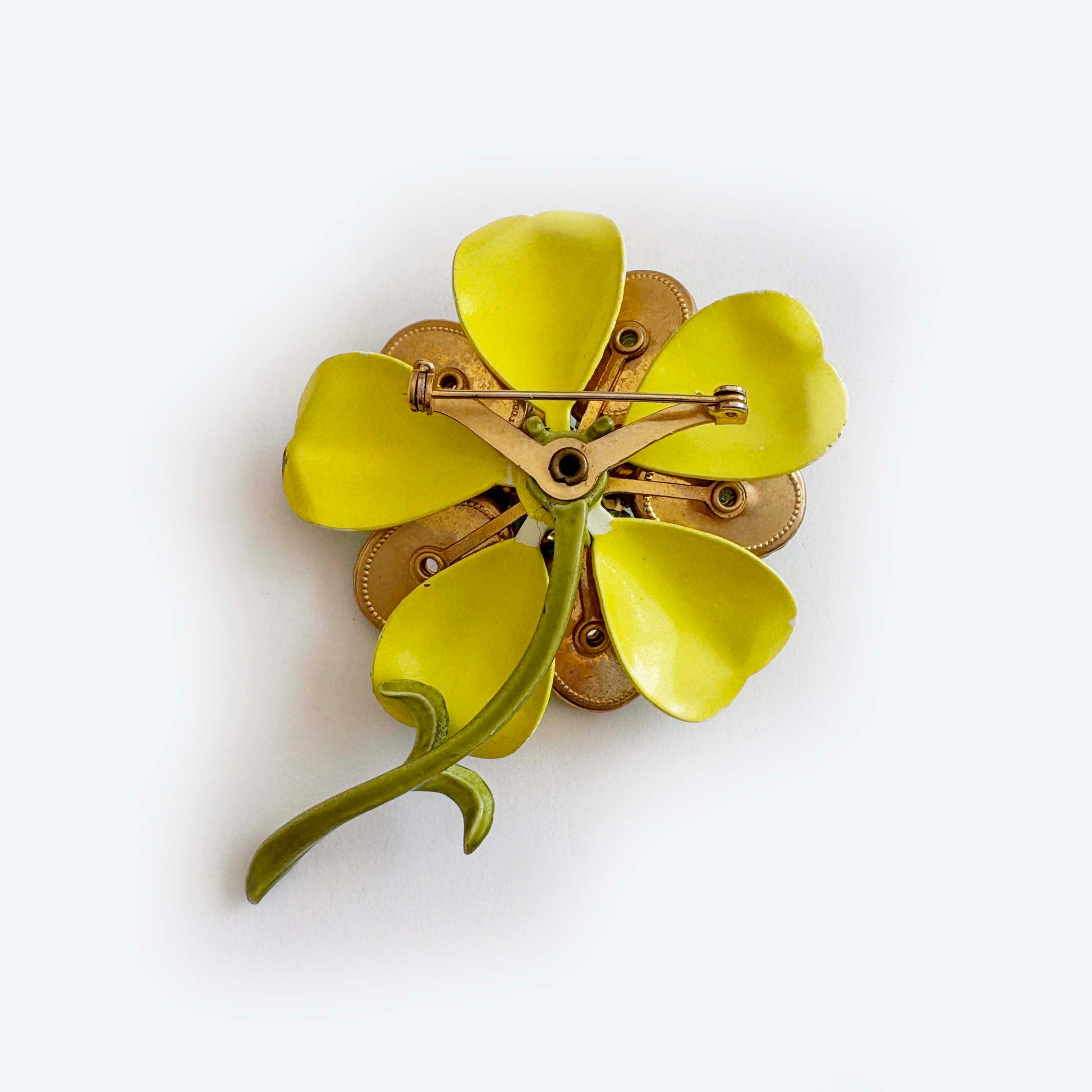 Floral brooch with yellow petals and gold accents on a white background