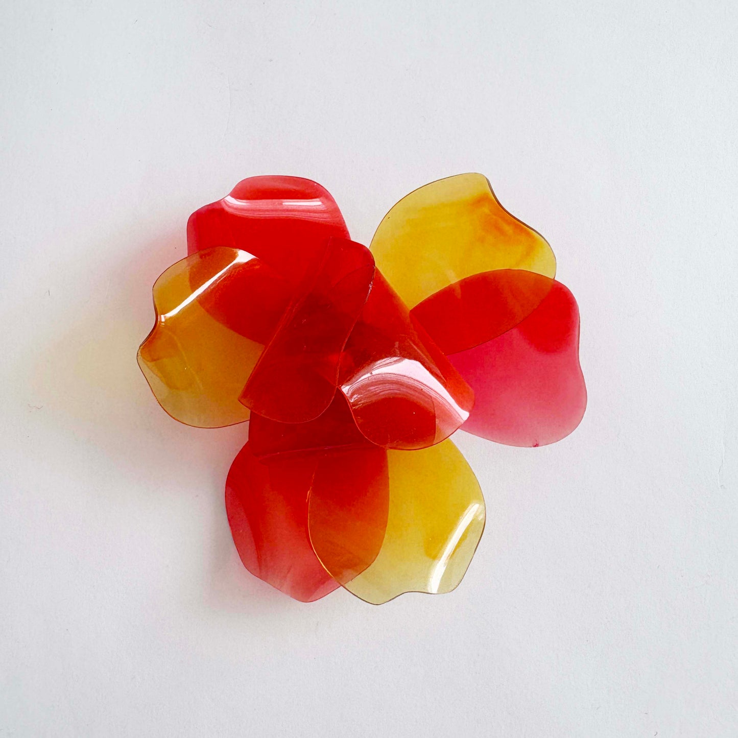 Vintage 1960s translucent red and yellow layered flower brooch made from cellulose acetate on a white background