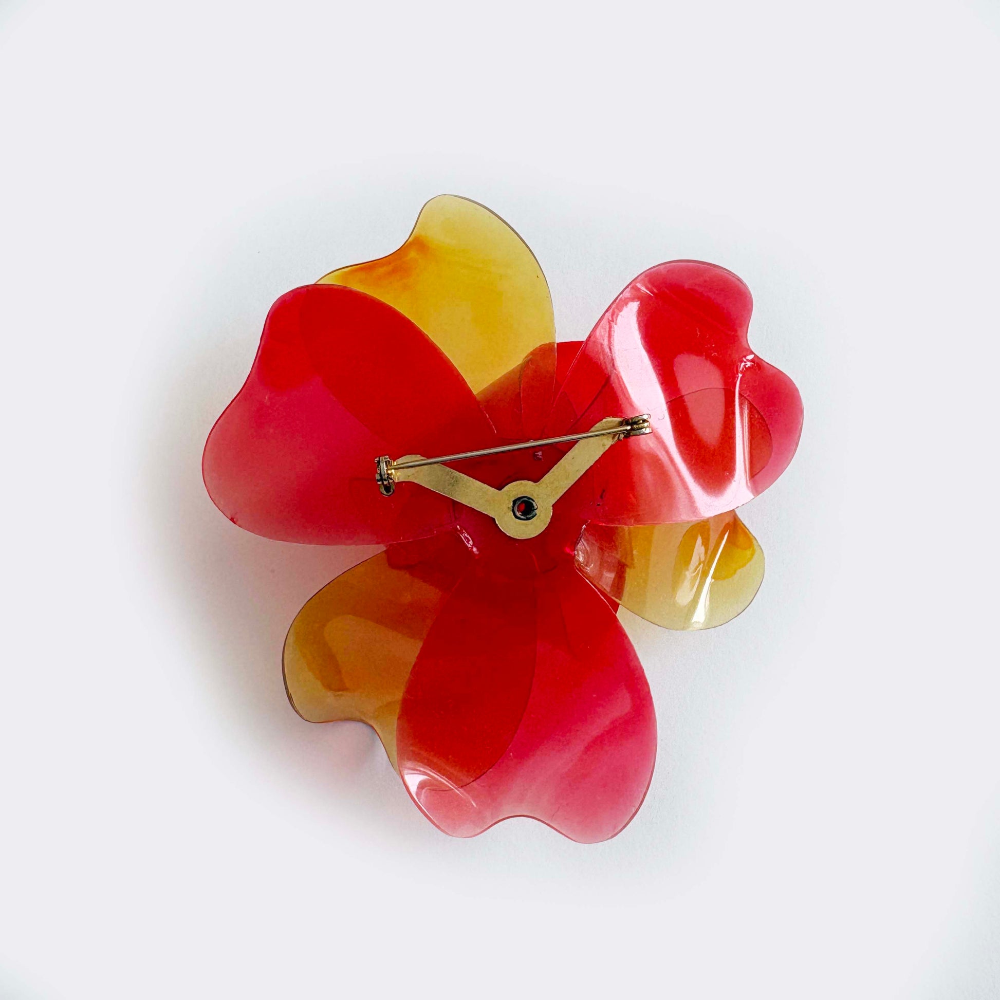 Vintage 1960s translucent red and yellow layered flower brooch made from cellulose acetate on a white background