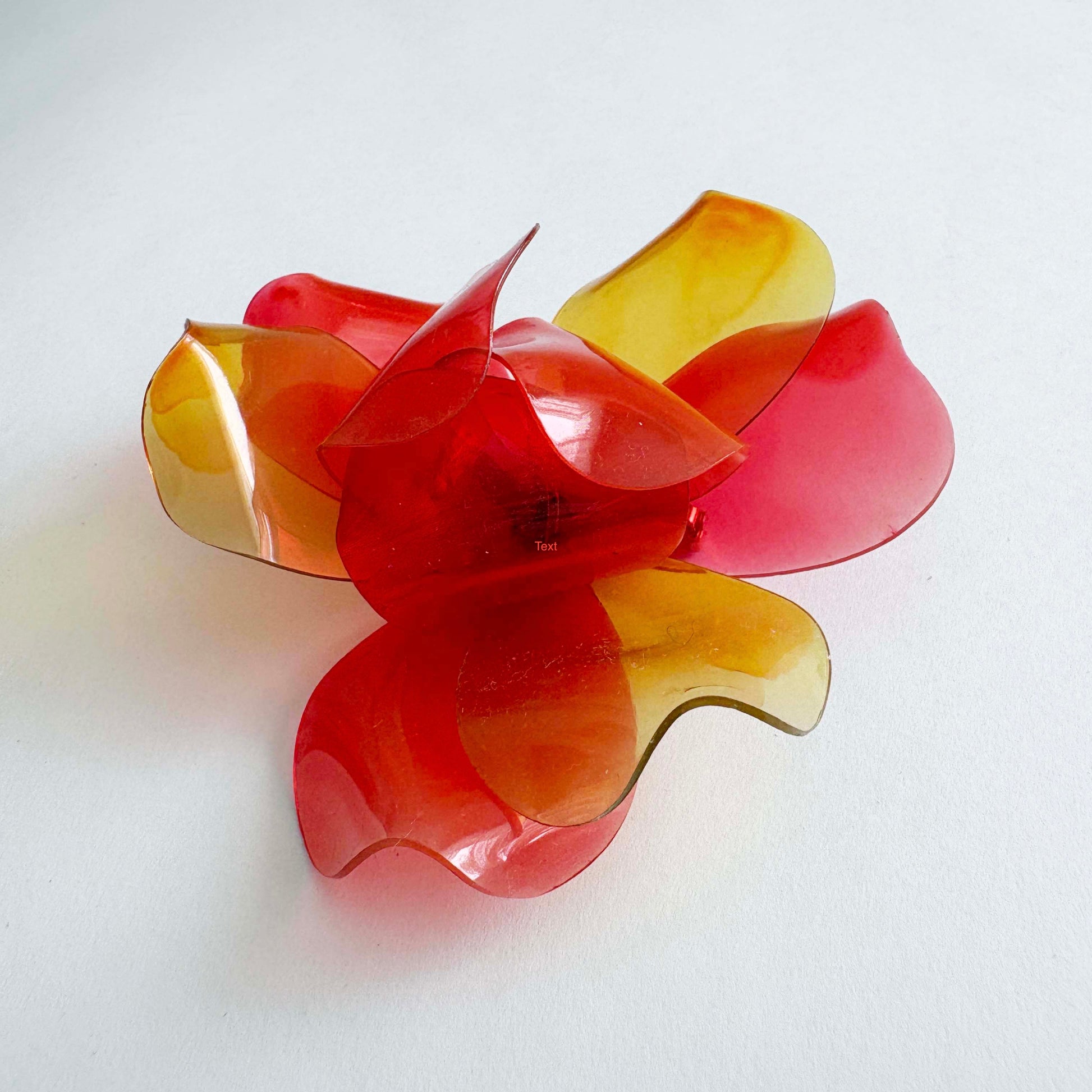 Vintage 1960s translucent red and yellow layered flower brooch made from cellulose acetate on a white background