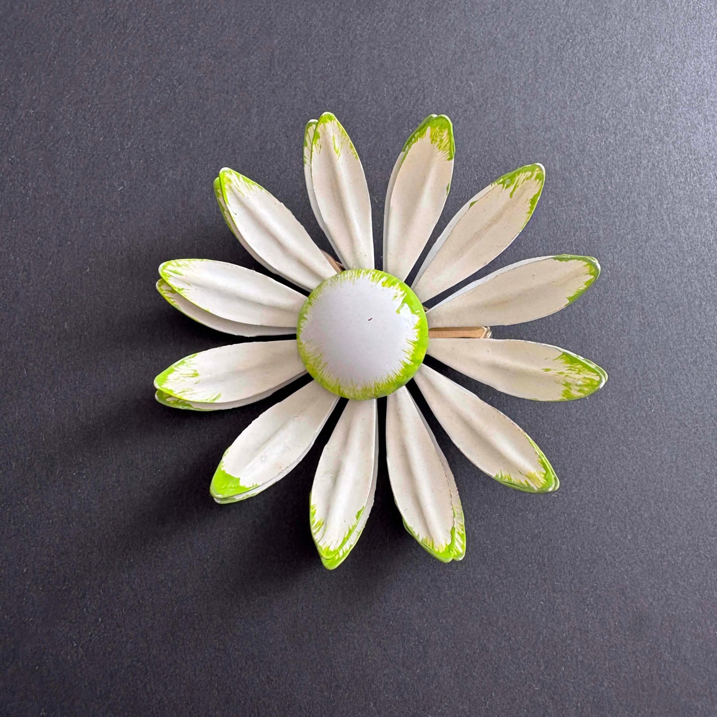 Vintage white enamel daisy brooch with green tipped petals, 1960s on black background