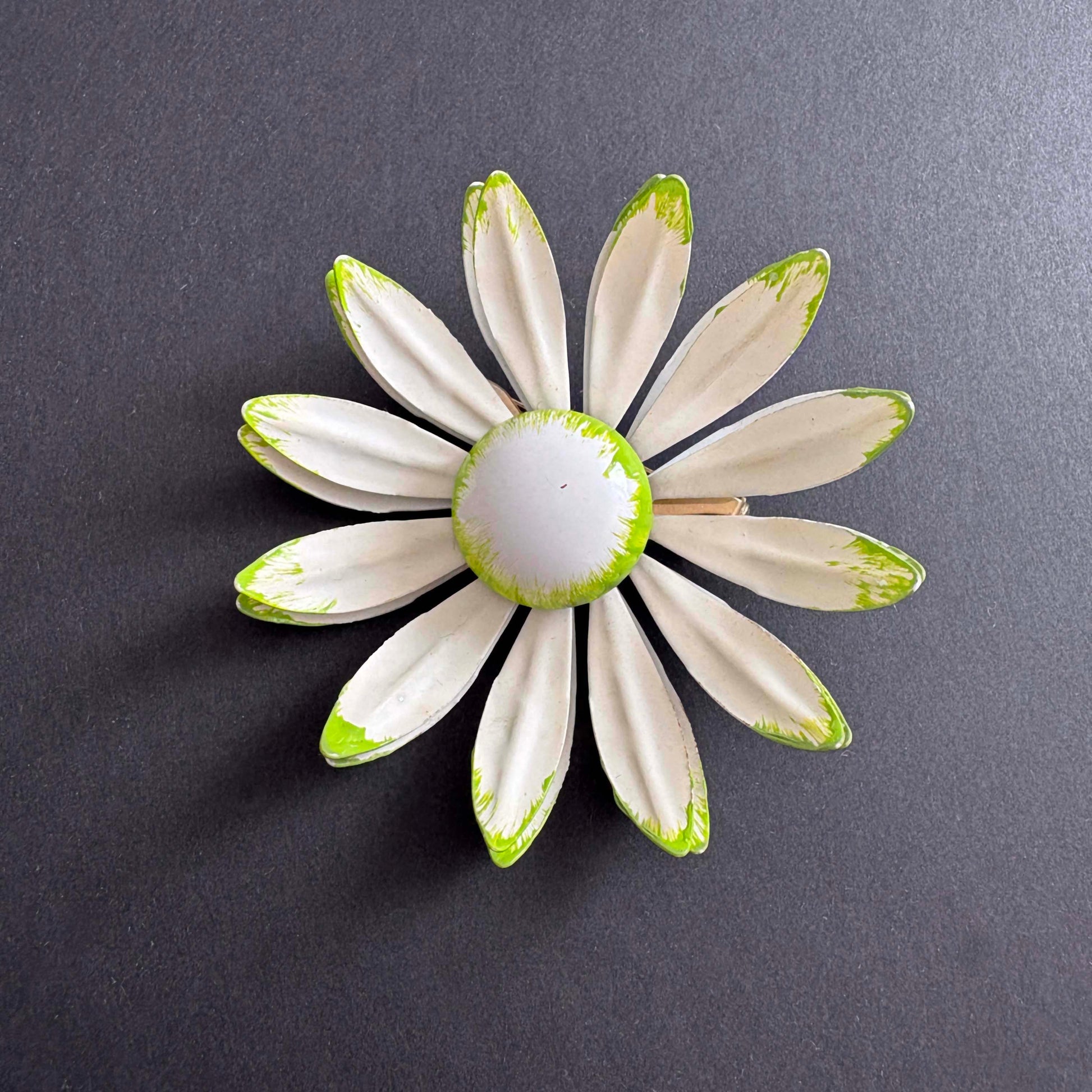 Vintage white enamel daisy brooch with green tipped petals, 1960s on black background