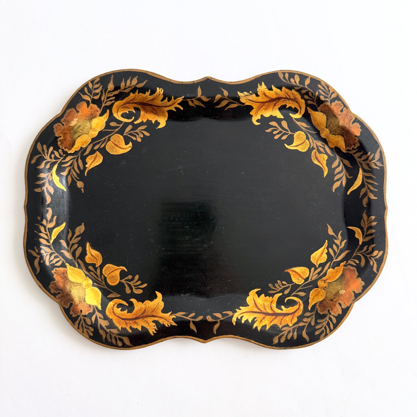 Vintage hand-painted toleware tray with gold floral design on black scalloped metal on white background
