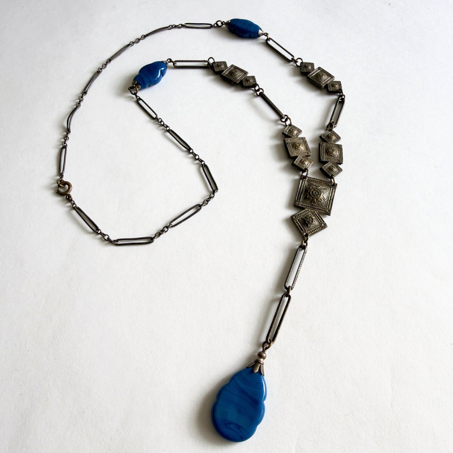 Vintage Czech Art Deco sautoir necklace featuring molded blue glass drops and geometric stamped panels. Bohemian glass jewelry from the 1920s–1930s.