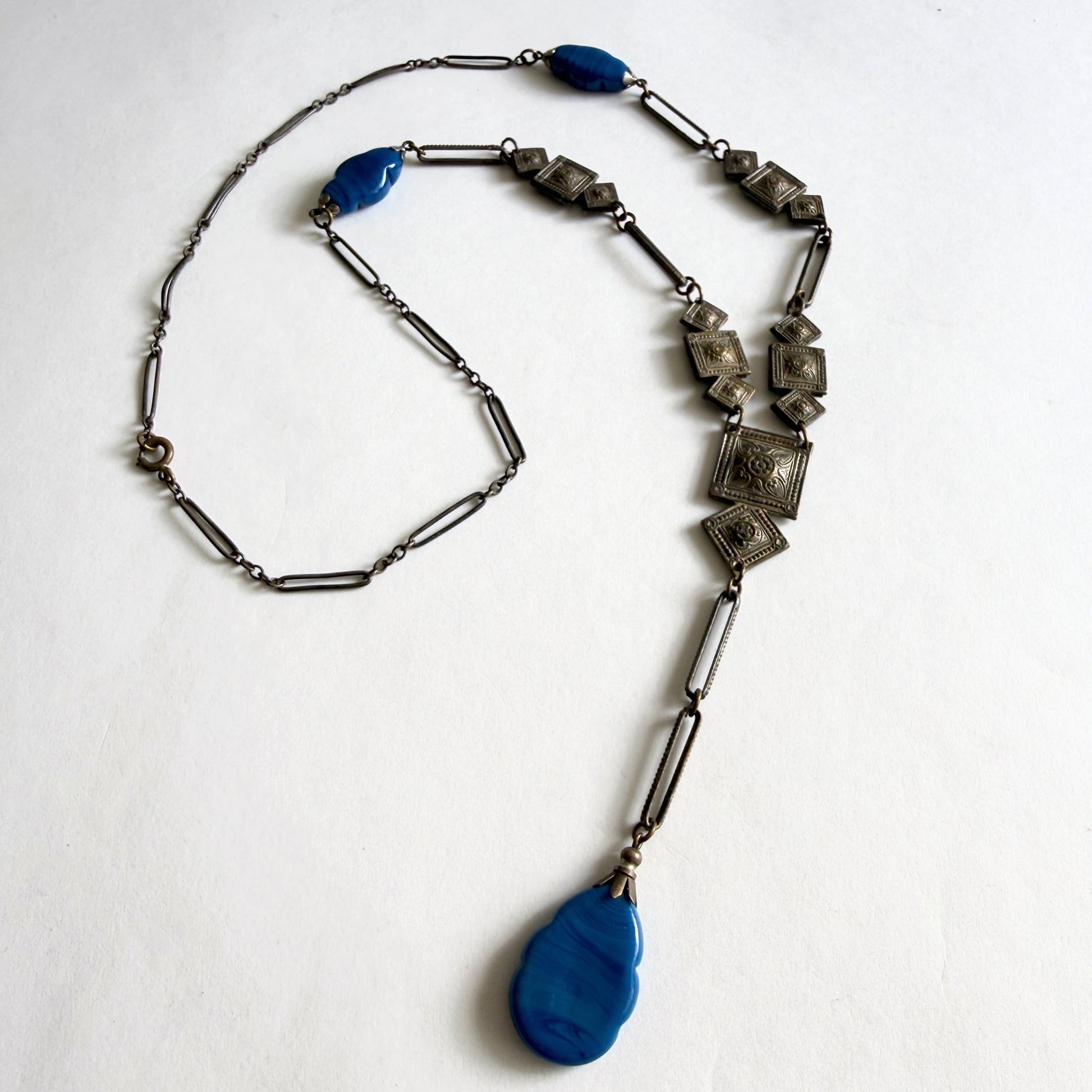 Vintage Czech Art Deco sautoir necklace featuring molded blue glass drops and geometric stamped panels. Bohemian glass jewelry from the 1920s–1930s.