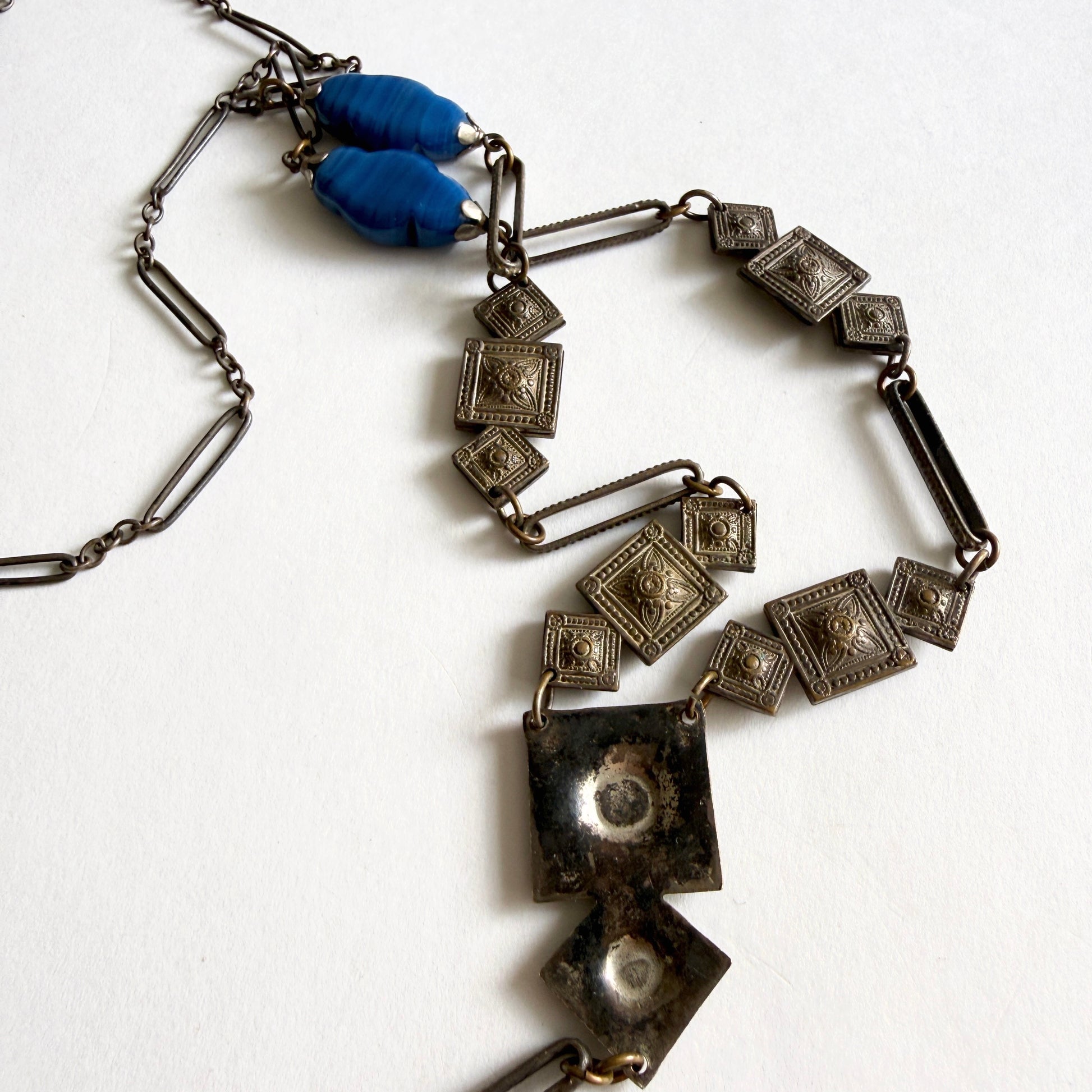 Vintage Czech Art Deco sautoir necklace with molded blue glass drop pendant and geometric stamped metal panels, circa 1920s–1930s.