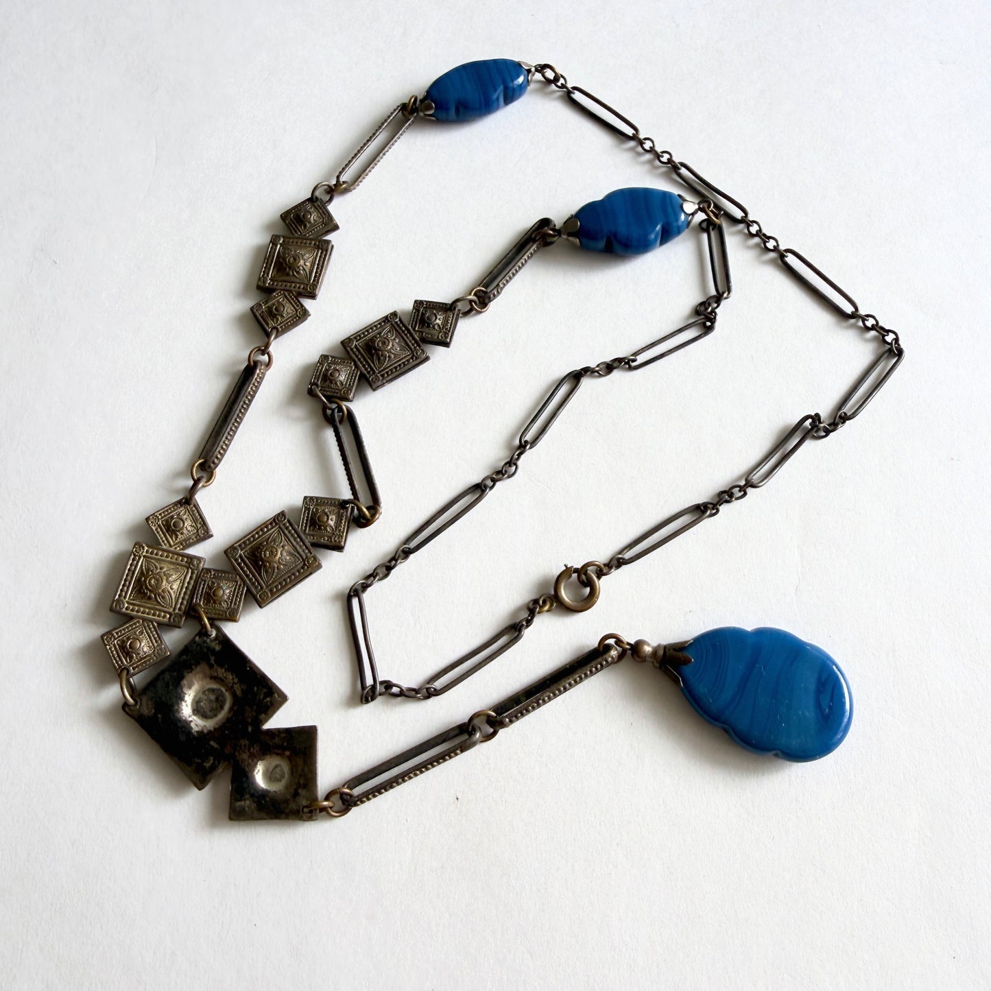 Vintage Czech Art Deco sautoir necklace with molded blue glass drop pendant and geometric stamped metal panels, circa 1920s–1930s.