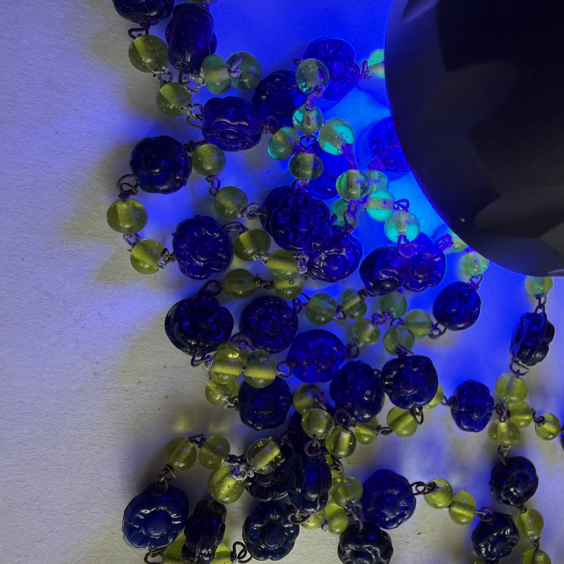 Blue and green beaded necklace on a white surface with uv lighting uranium glow