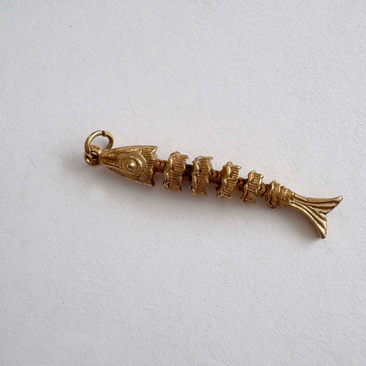 Vintage articulated gold-tone fish skeleton charm with movable segments, 1970s novelty jewelry on white background