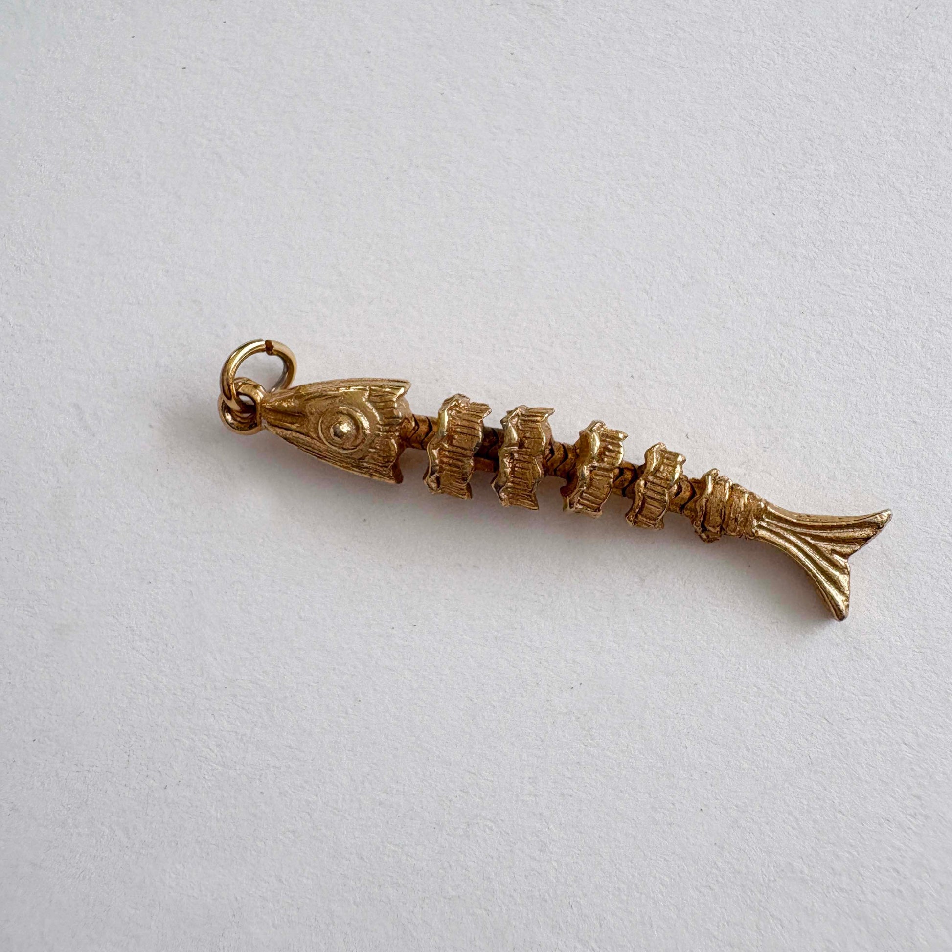 Vintage articulated gold-tone fish skeleton charm with movable segments, 1970s novelty jewelry on white background