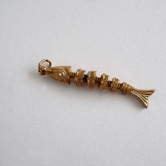 Vintage articulated gold-tone fish skeleton charm with movable segments, 1970s novelty jewelry on white background
