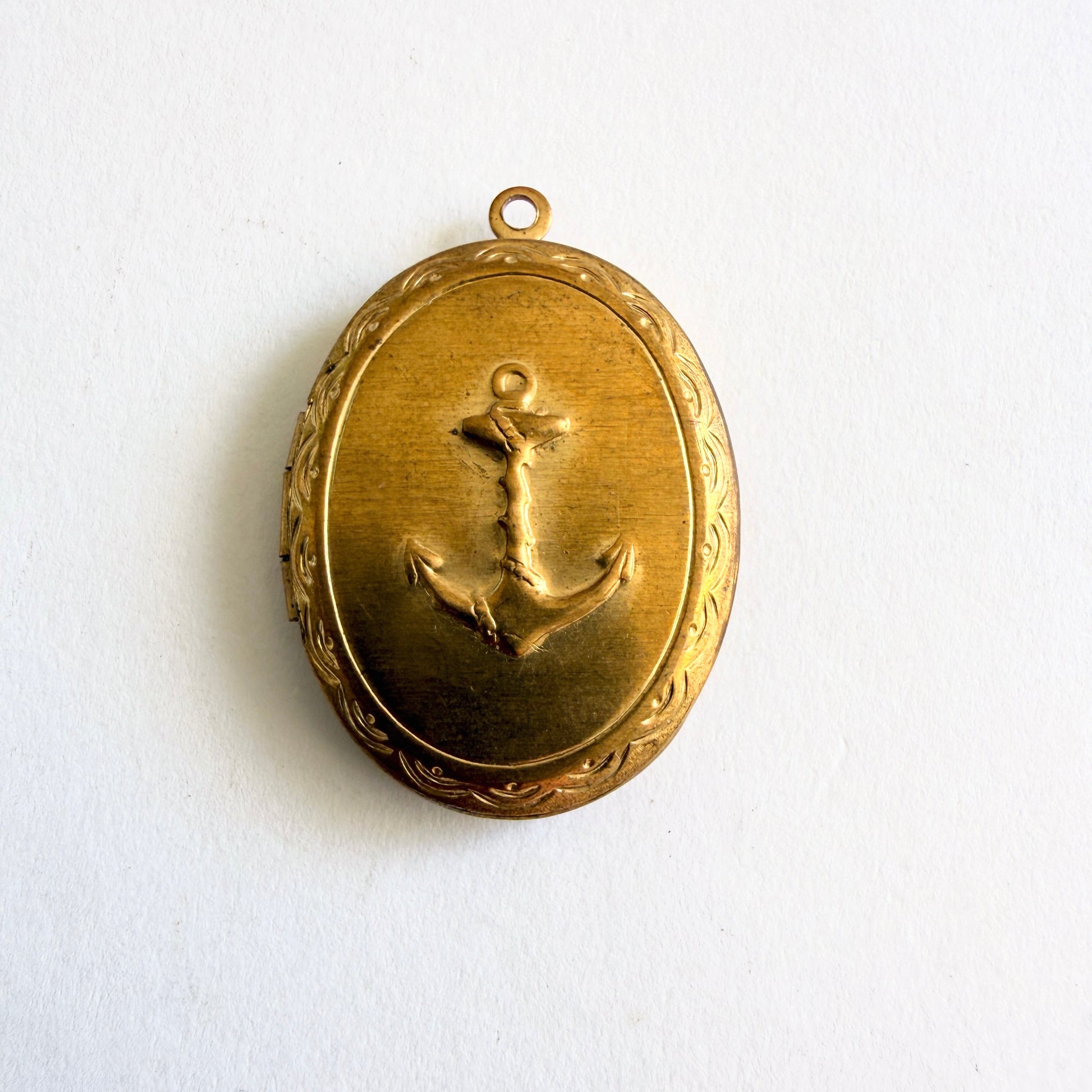Vintage gold tone oval locket with raised anchor motif and hinged opening showing dual photo compartments, circa 1960s