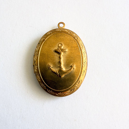 Vintage gold tone oval locket with raised anchor motif and hinged opening showing dual photo compartments, circa 1960s