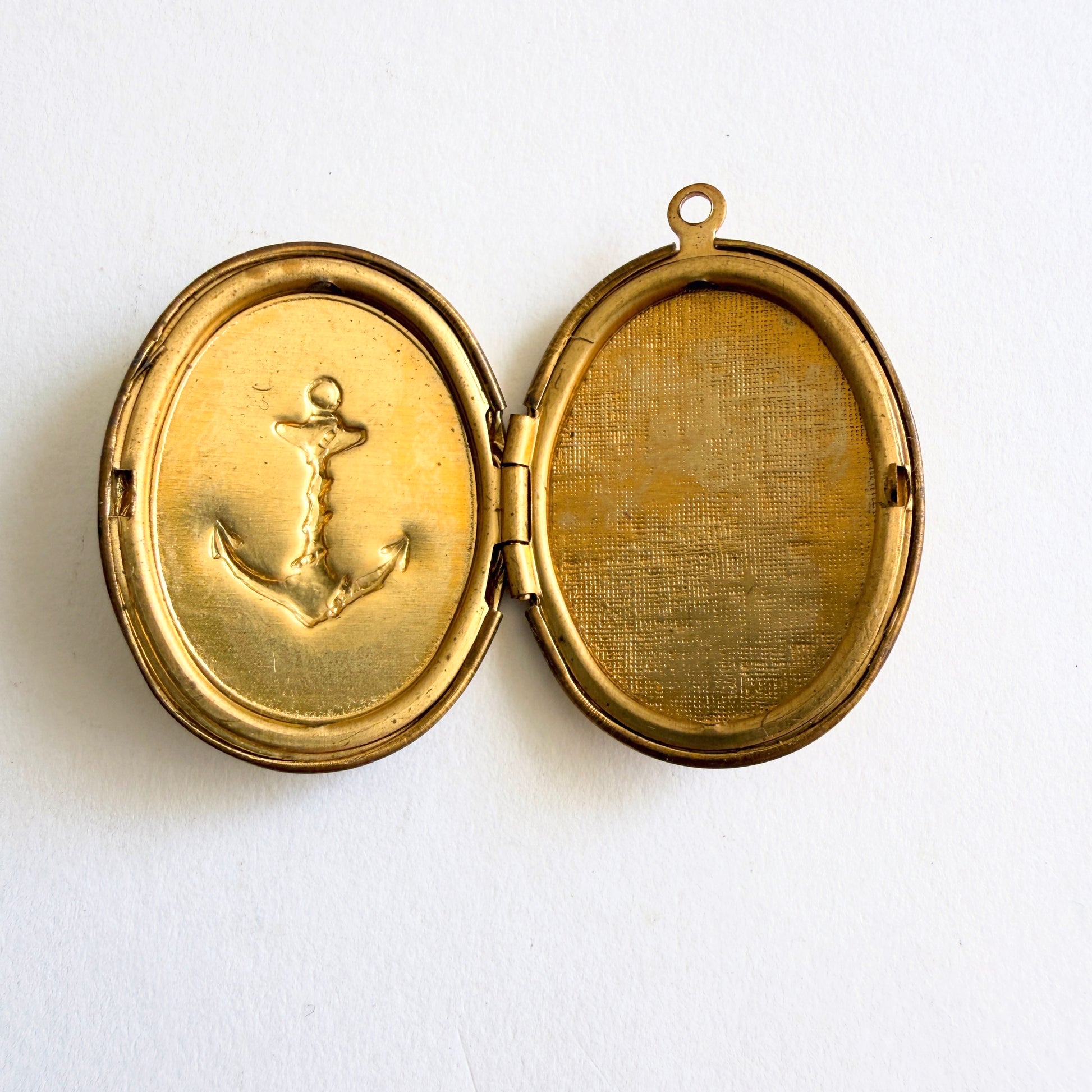 Vintage gold tone oval locket with raised anchor motif and hinged opening showing dual photo compartments, circa 1960s
