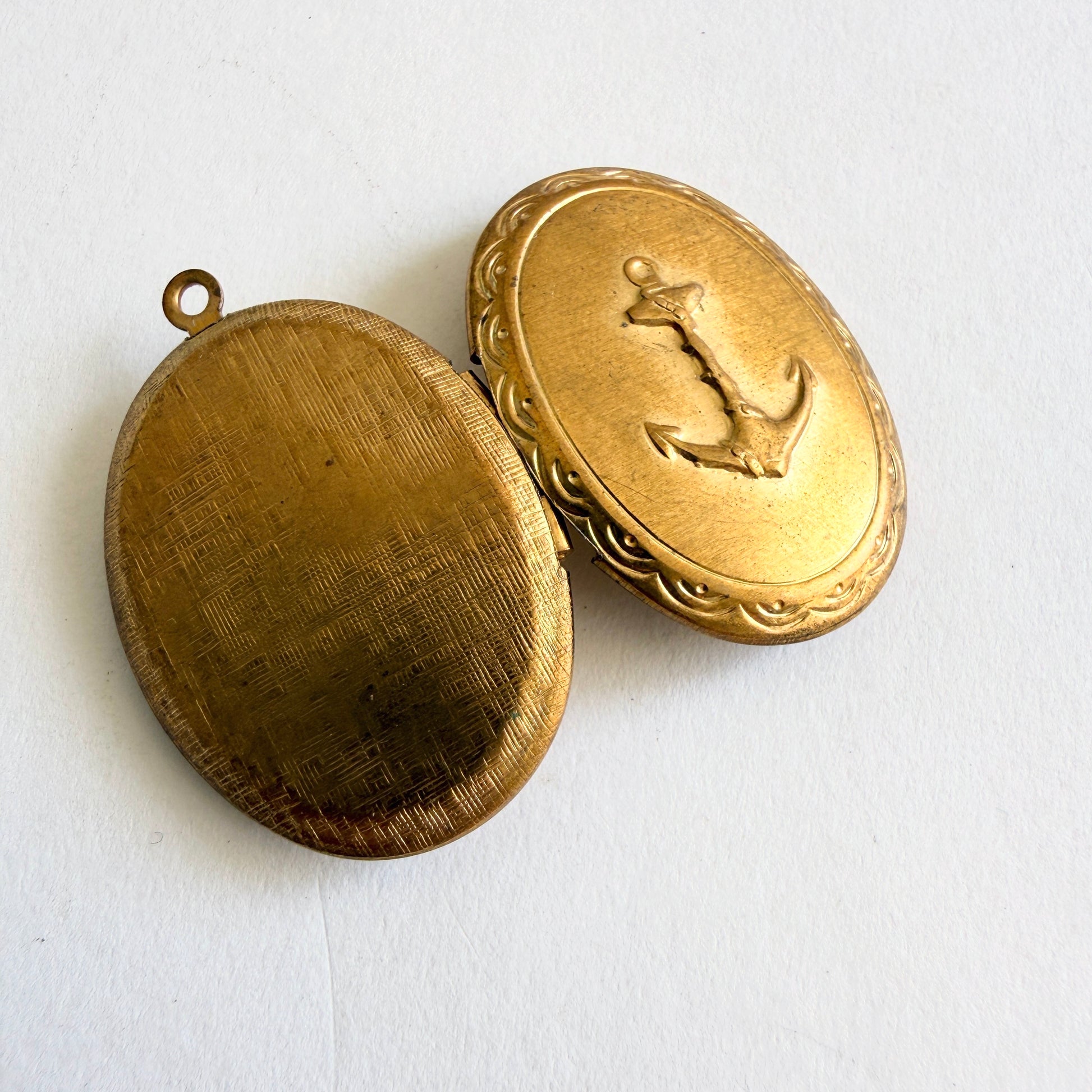 Vintage gold tone oval locket with raised anchor motif and hinged opening showing dual photo compartments, circa 1960s