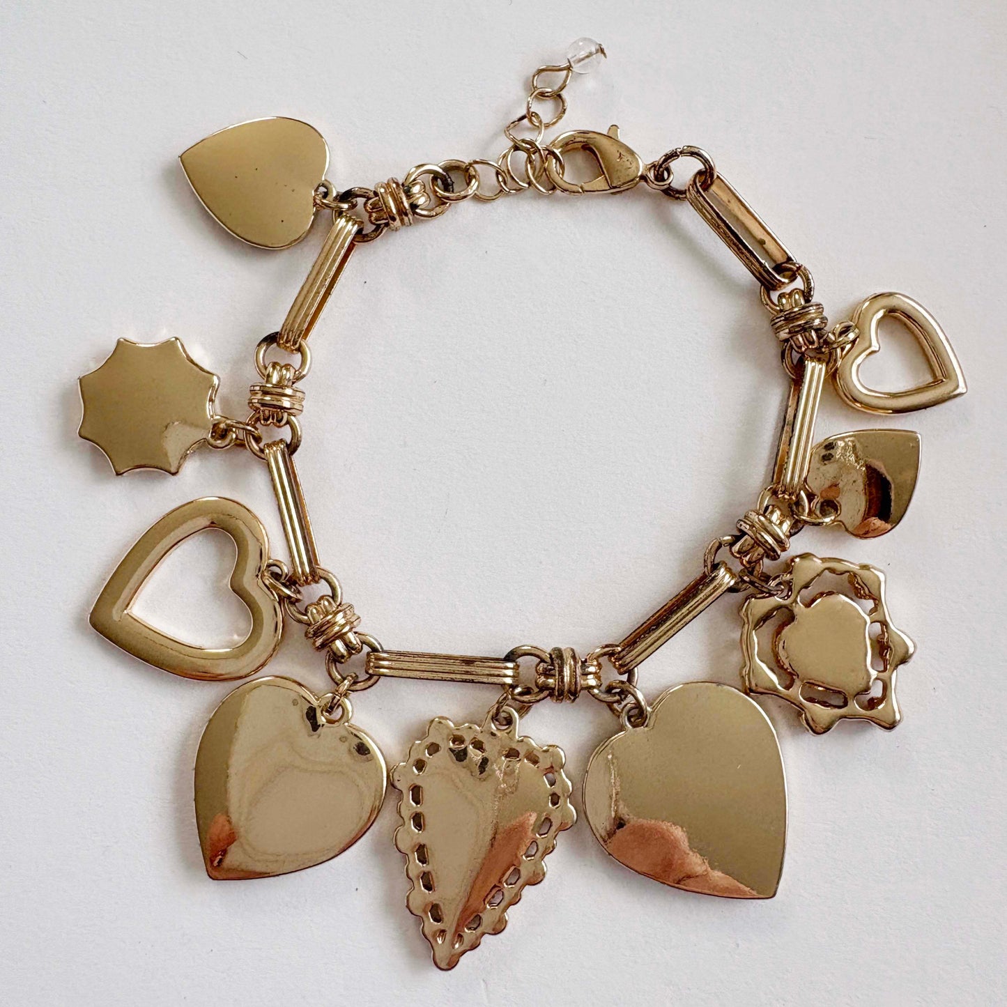 Gold charm bracelet with heart-shaped pendants on a white background