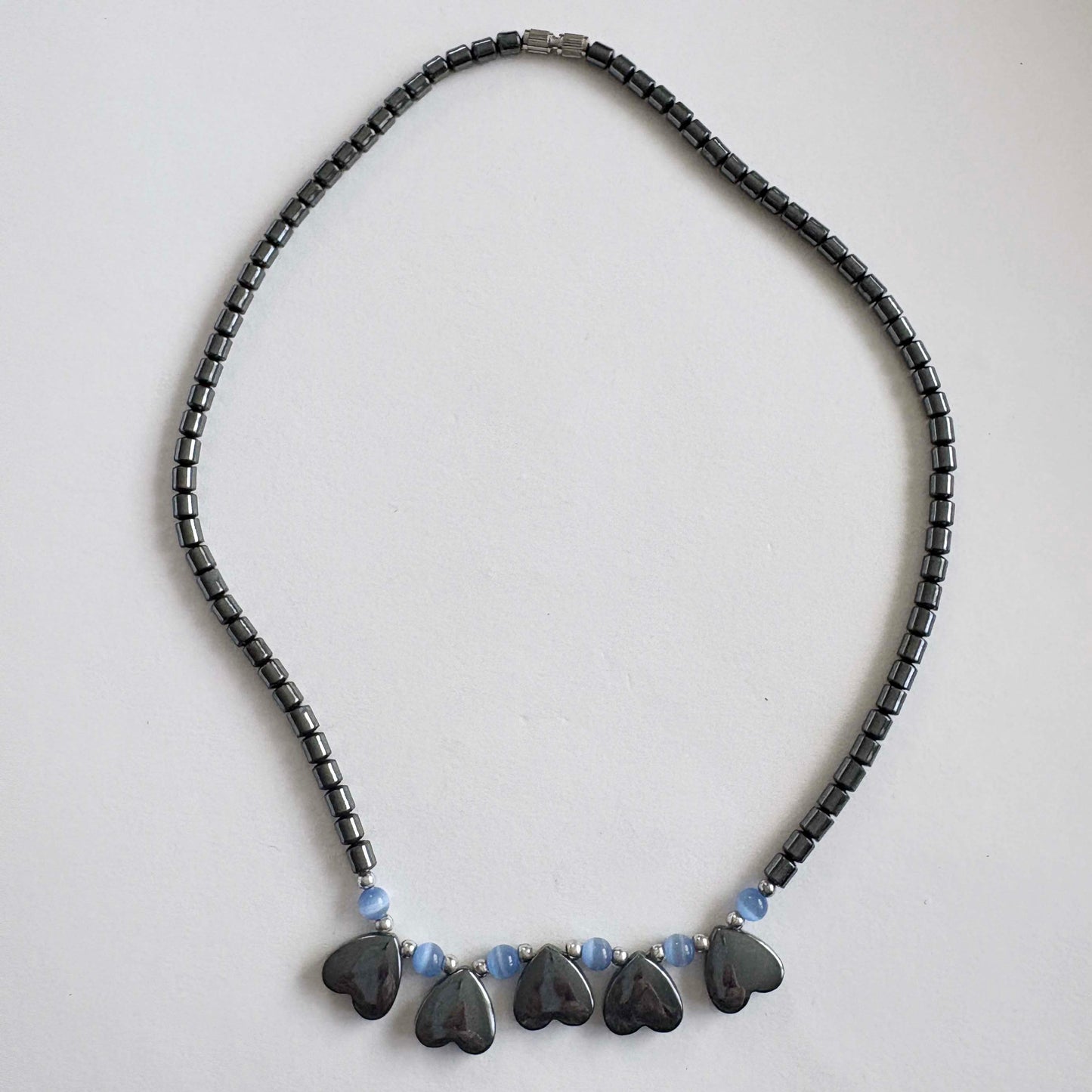 Necklace with black beads and heart-shaped pendants on a light gray background