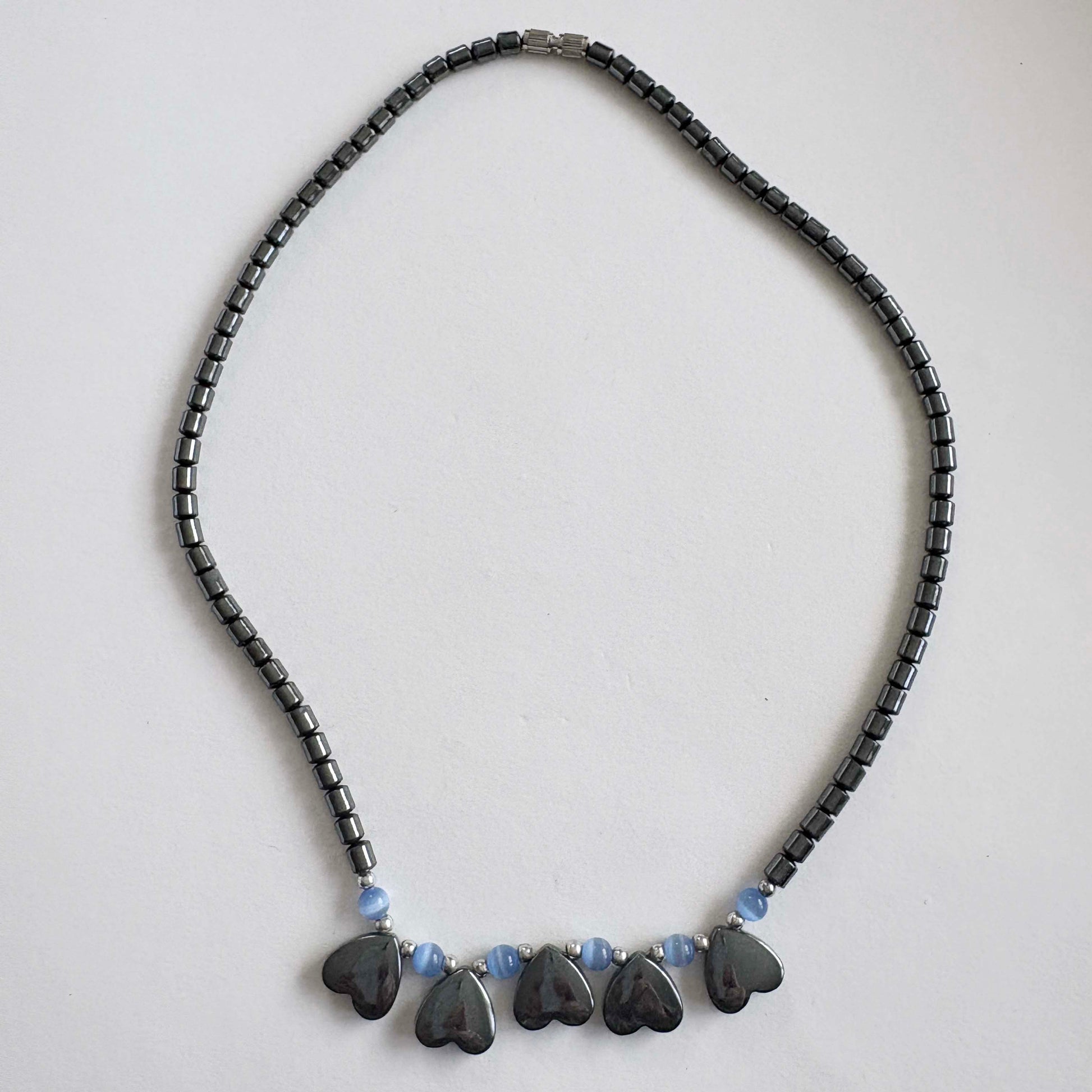 Necklace with black beads and heart-shaped pendants on a light gray background