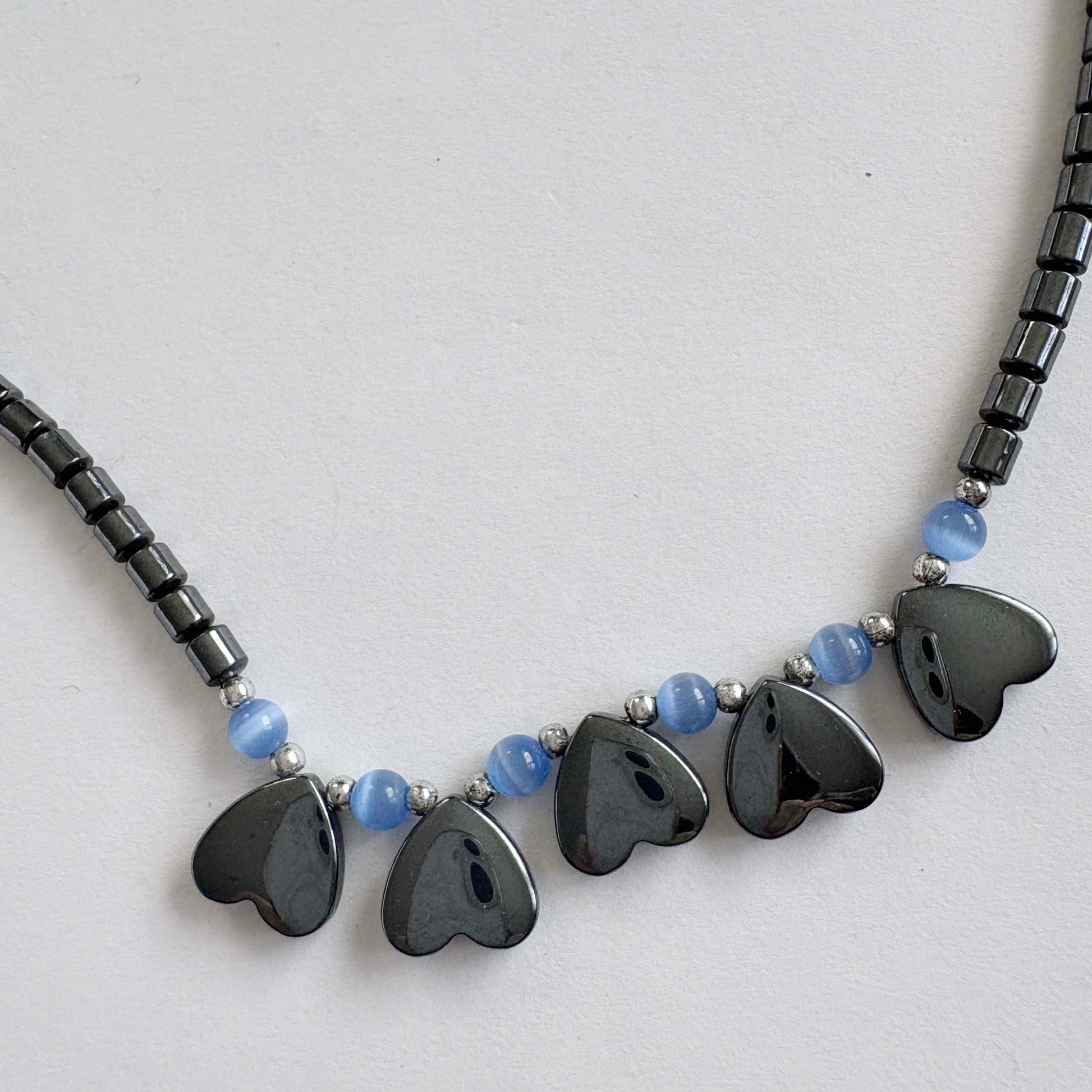 Necklace with heart-shaped black beads and blue accents on a light gray background