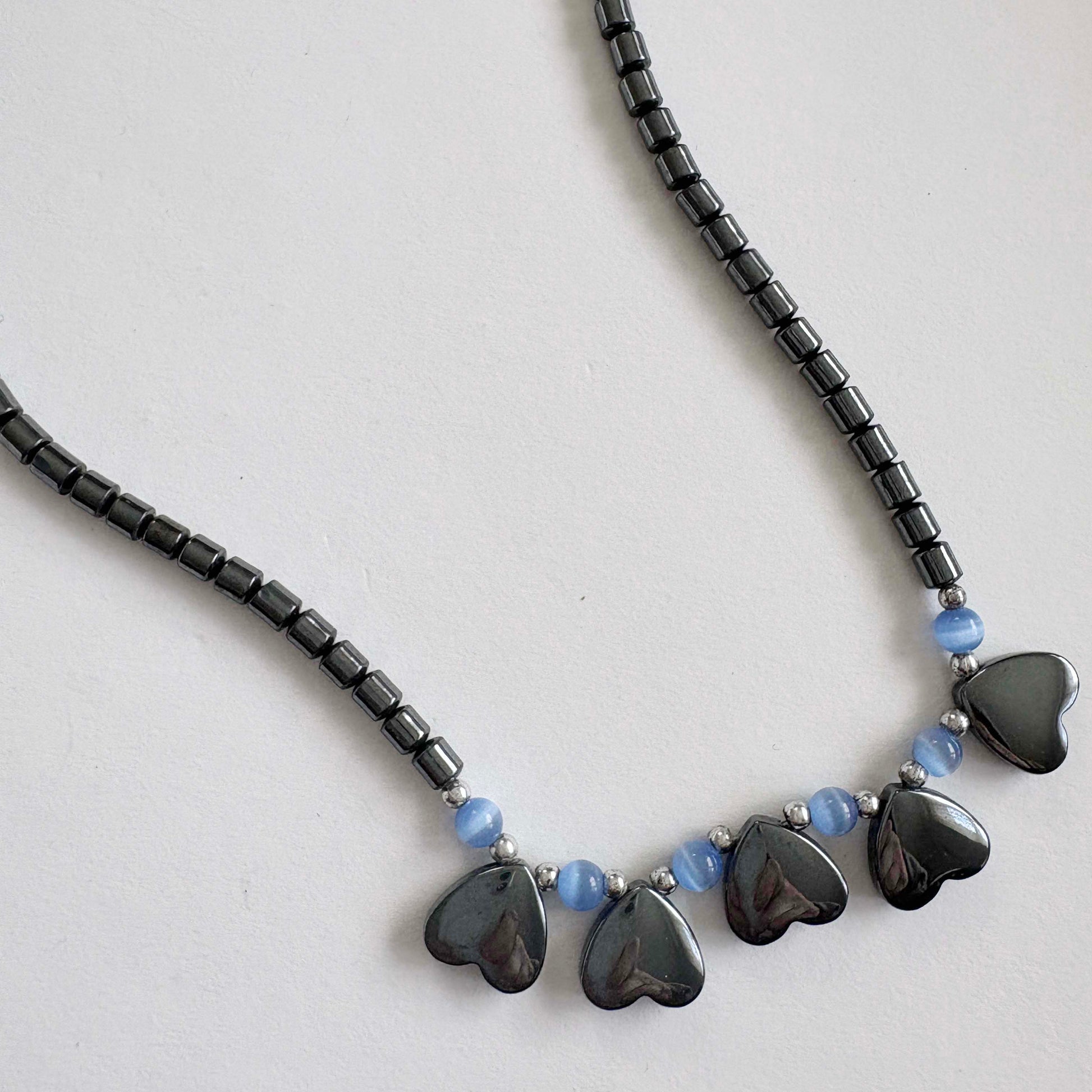 Necklace with black heart-shaped beads and blue beads on a light gray background