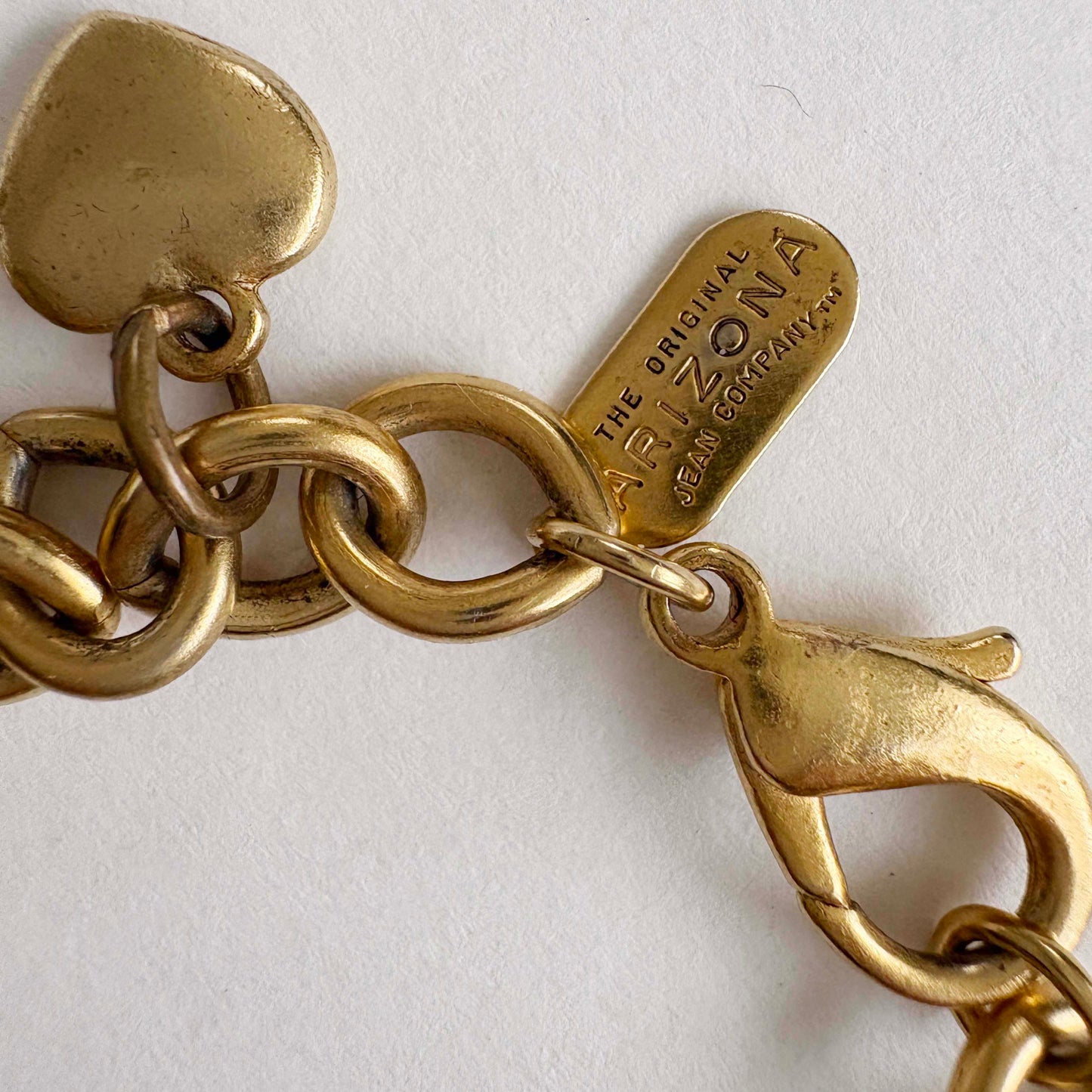 Gold chain bracelet with a clasp and 'The Original Arizona Jean Company' tag on a white background