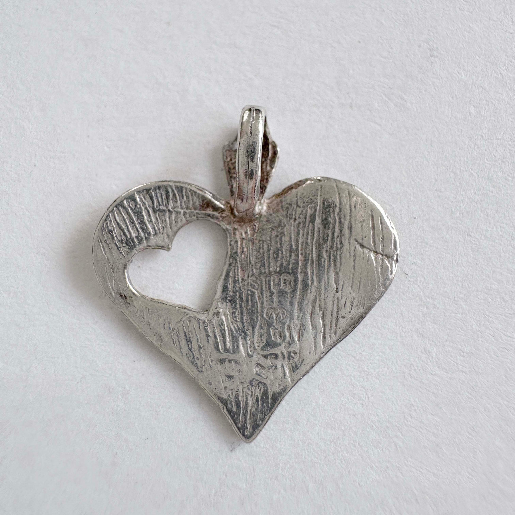 Vintage sterling silver heart charm with cut-out heart detail on white background