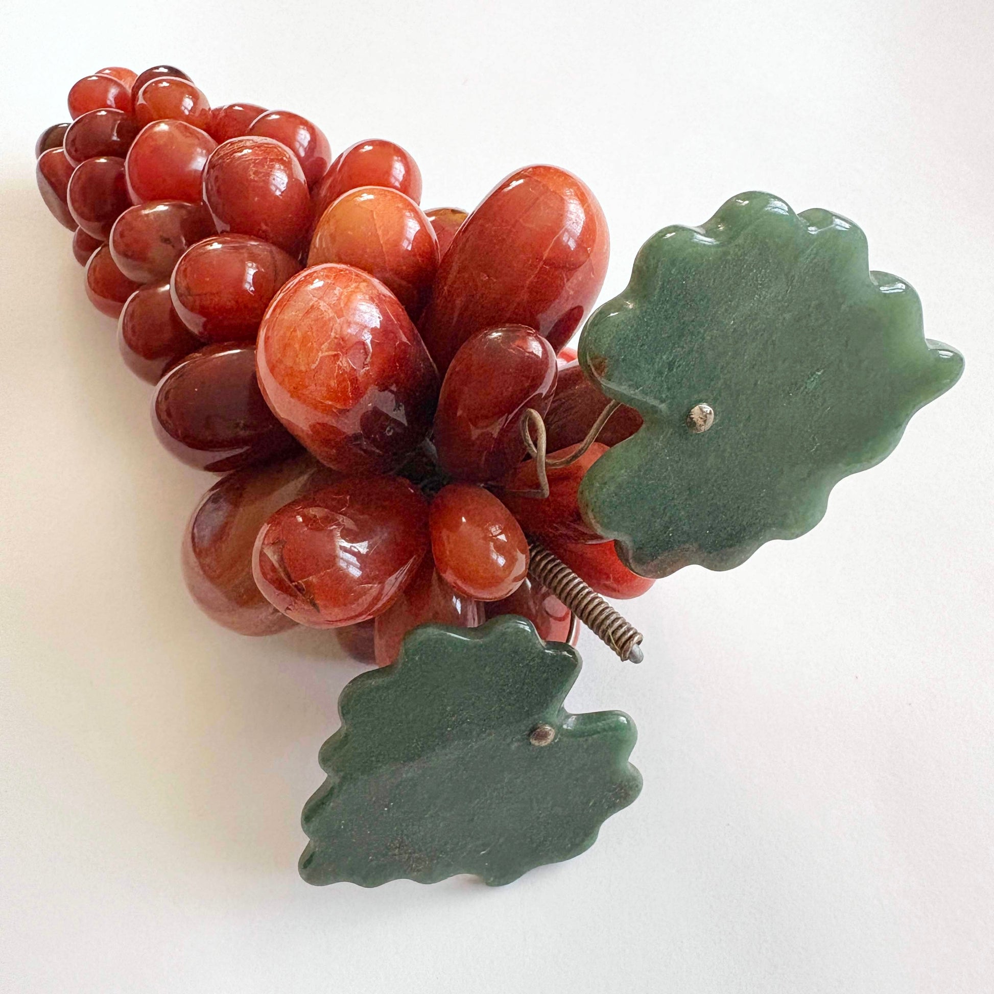 Decorative red stone grapes and green leaves on a white background