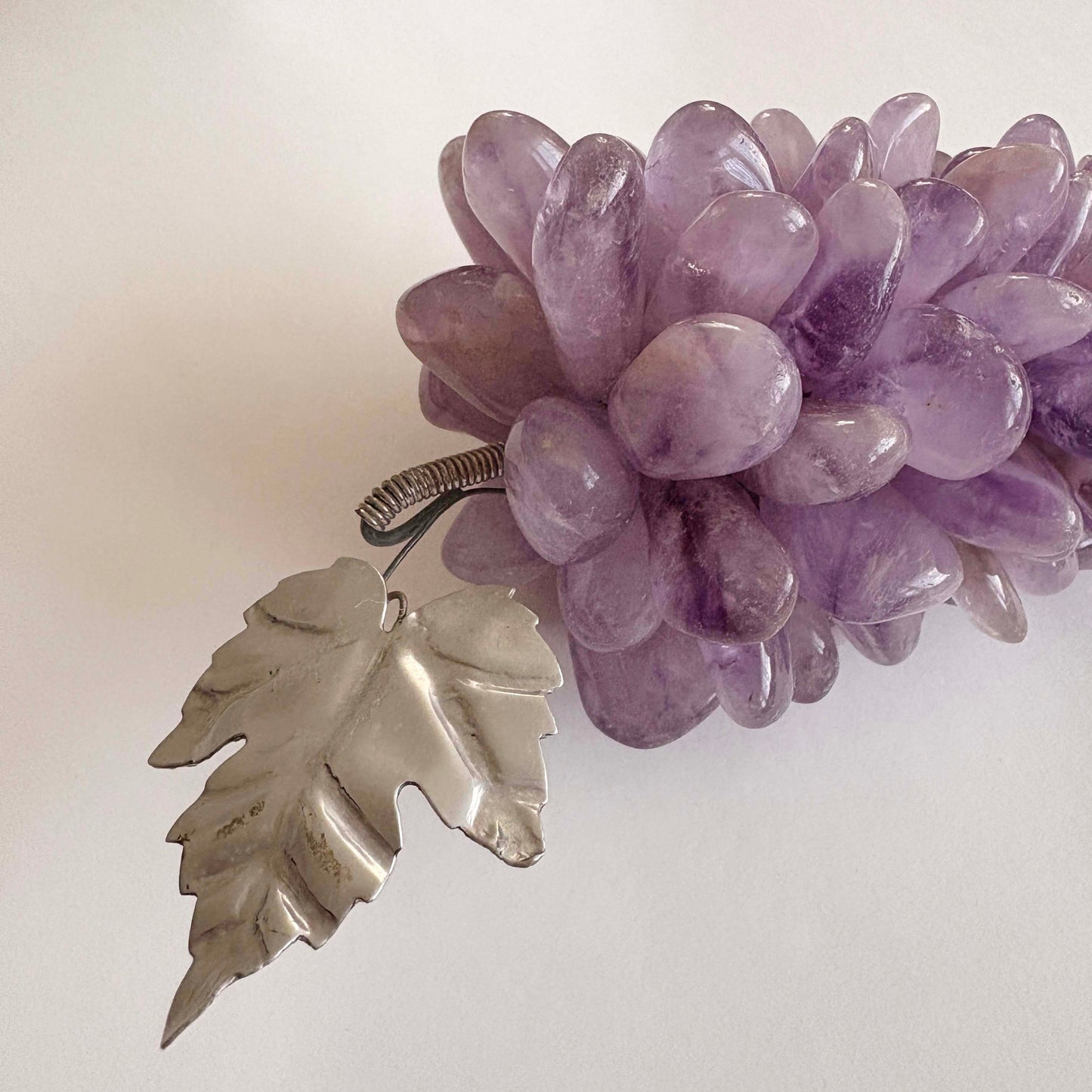Purple stone grapes with a silver leaf pendant on a light background