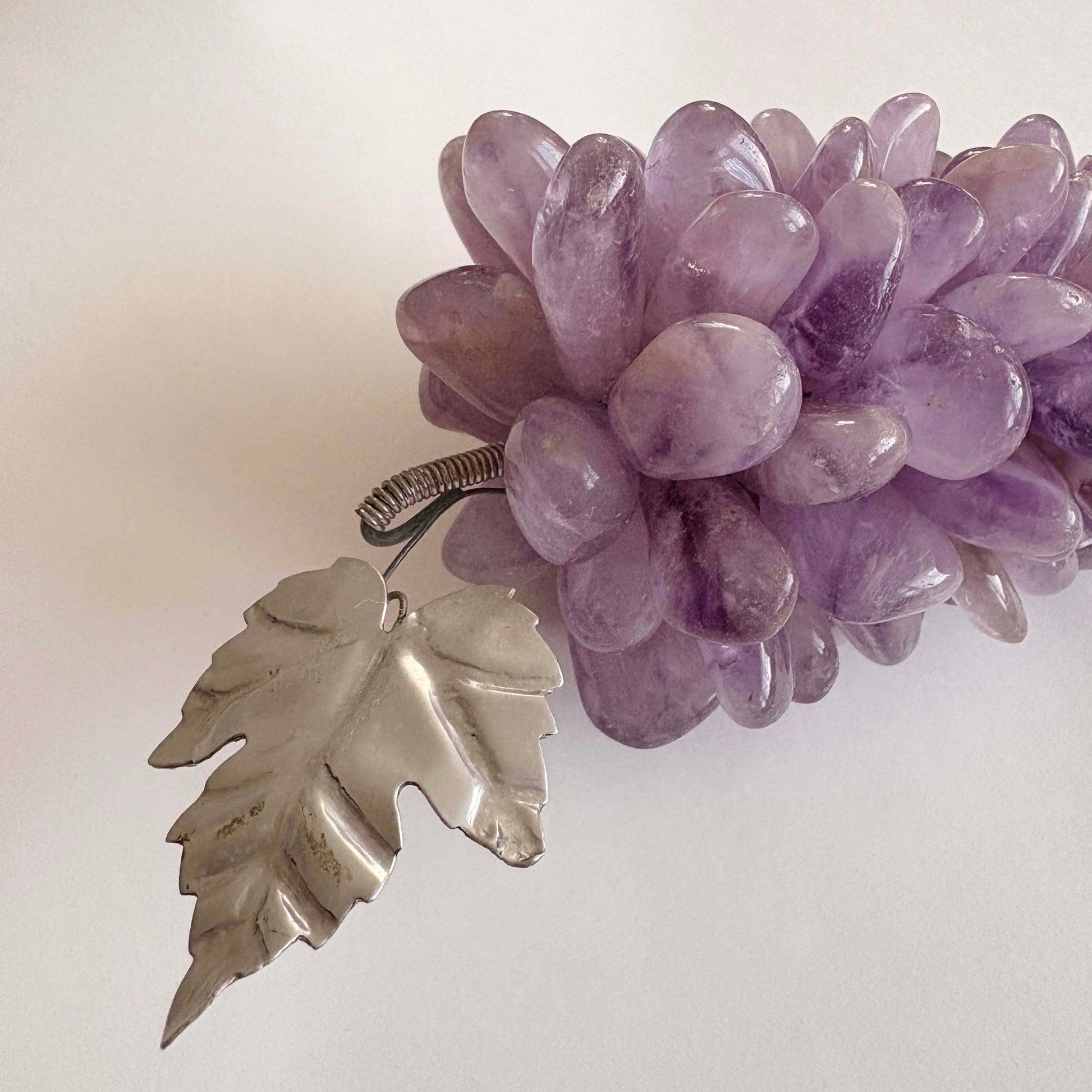 Purple stone grapes with a silver leaf pendant on a light background