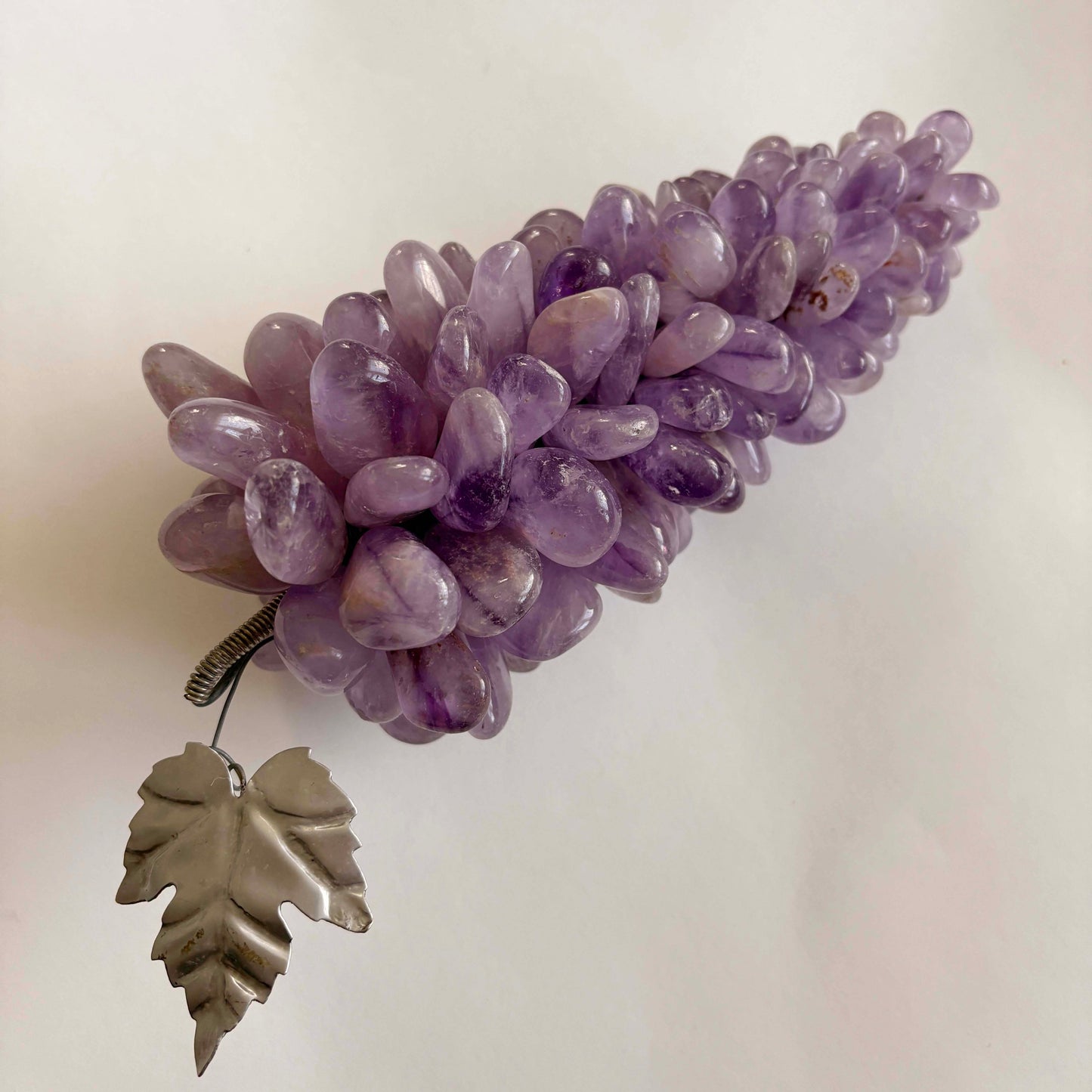 Amethyst cluster of grapes with a silver leaf on a light background